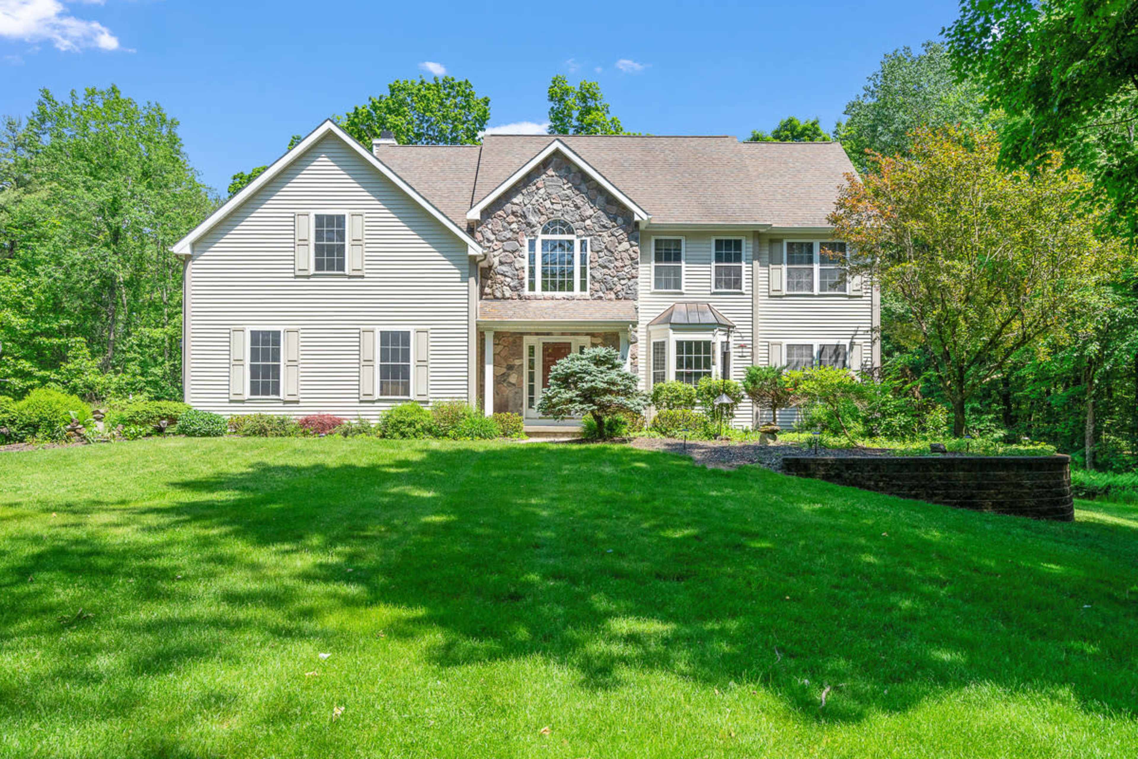 A large, two-story house with a stone accent facade is set in a well-maintained lawn surrounded by trees.