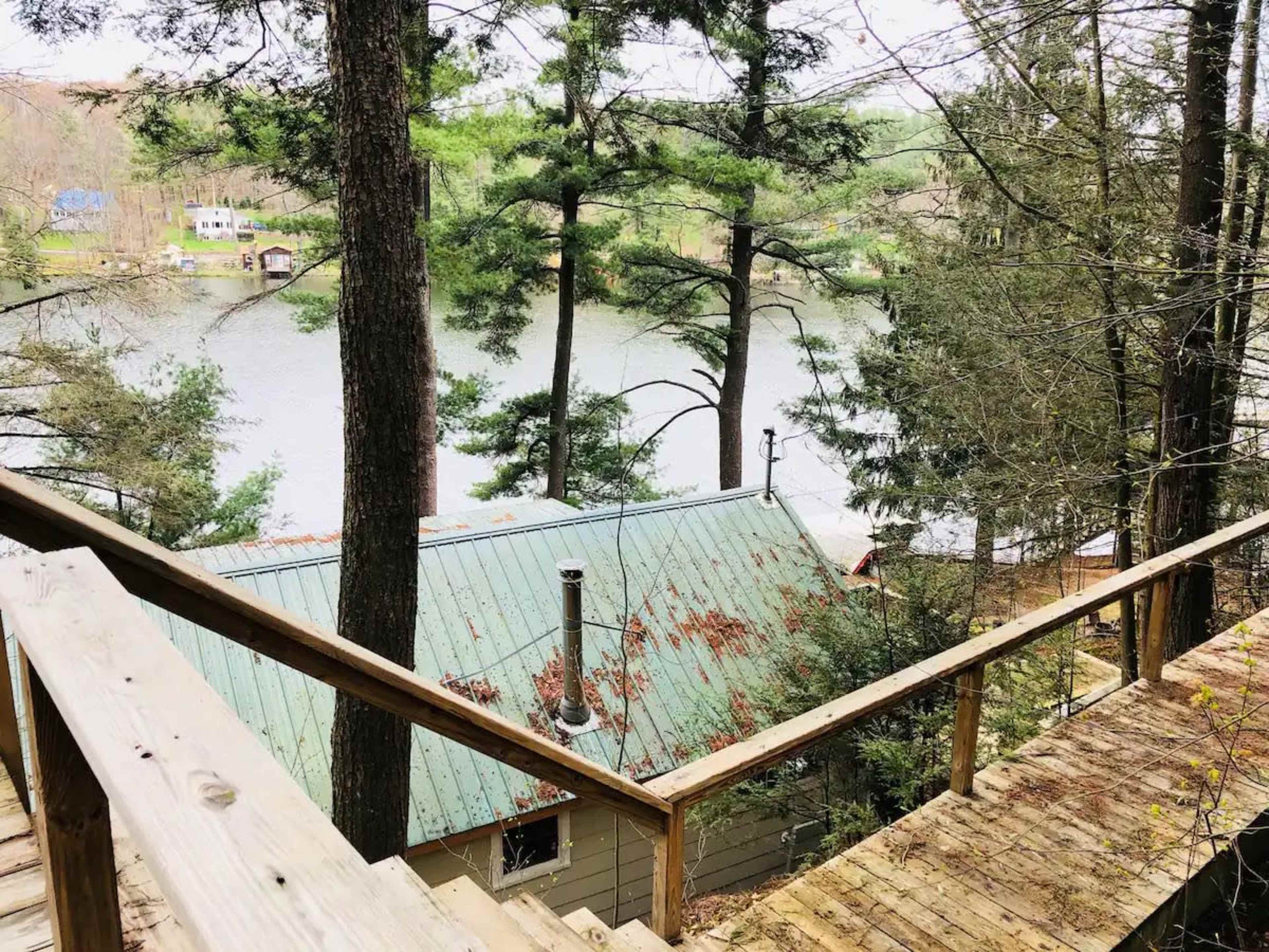 A wooden staircase leads down to a lakeside cabin surrounded by tall trees and a calm body of water.