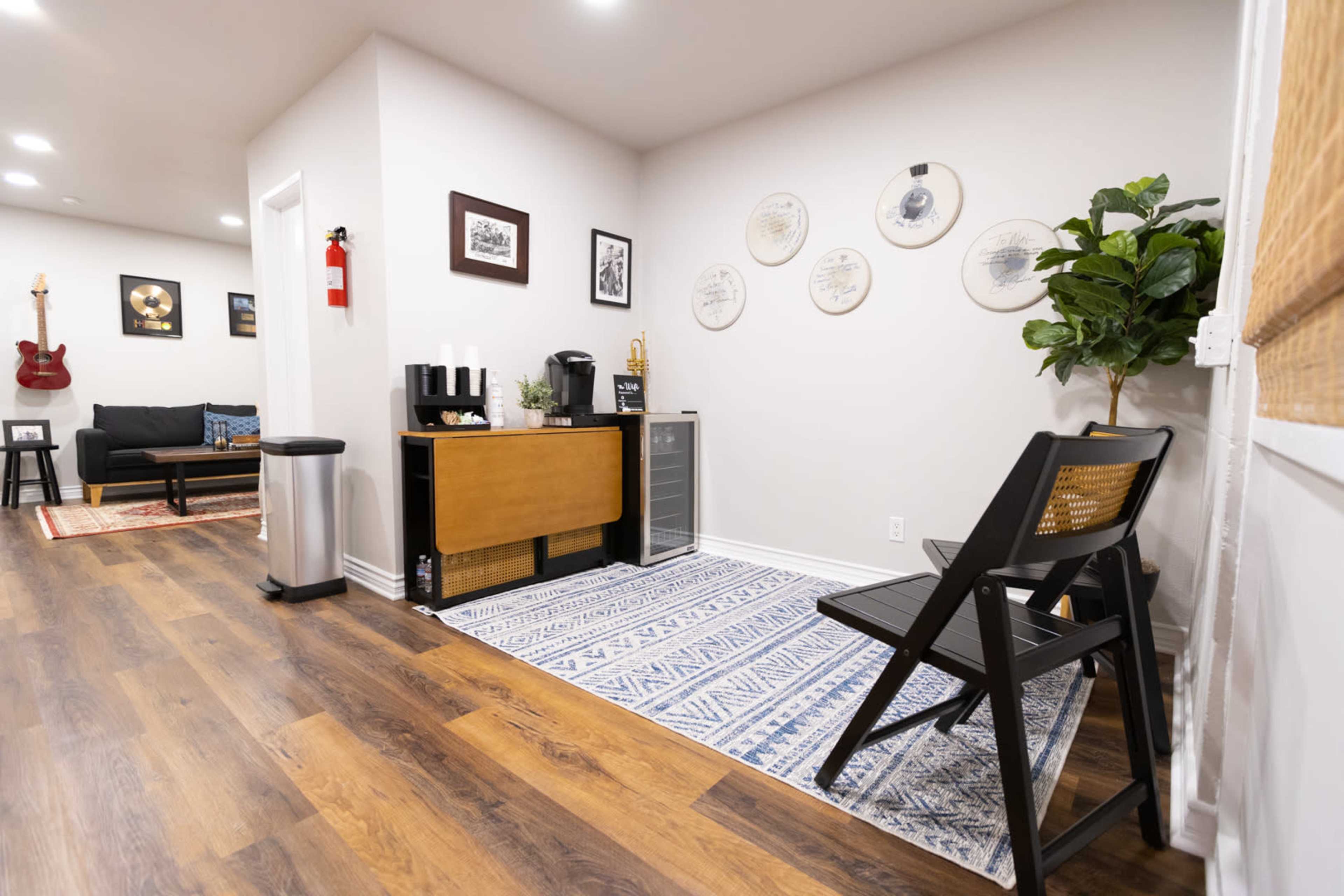 The image shows a modern, well-lit interior space featuring a seating area with a sofa, a coffee station, and decorative wall art.