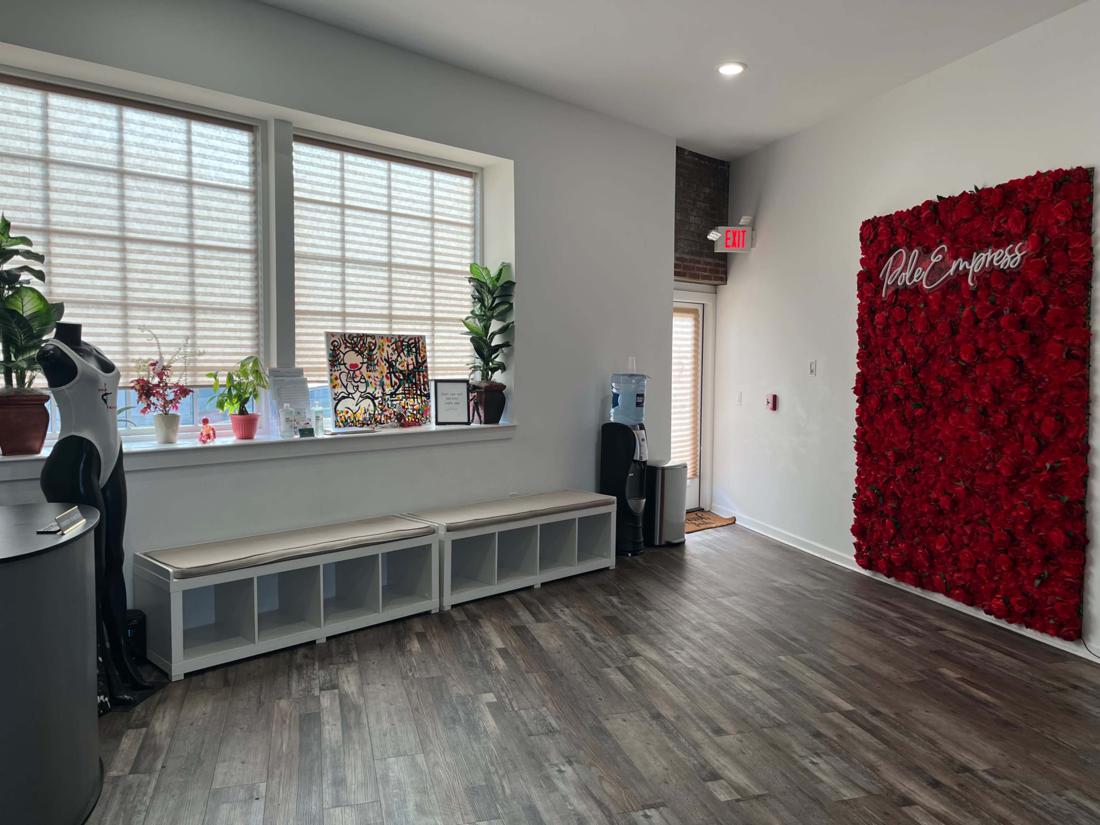 The image shows a spacious interior with a floral wall decoration, seating area with storage cubbies, and windows allowing natural light.