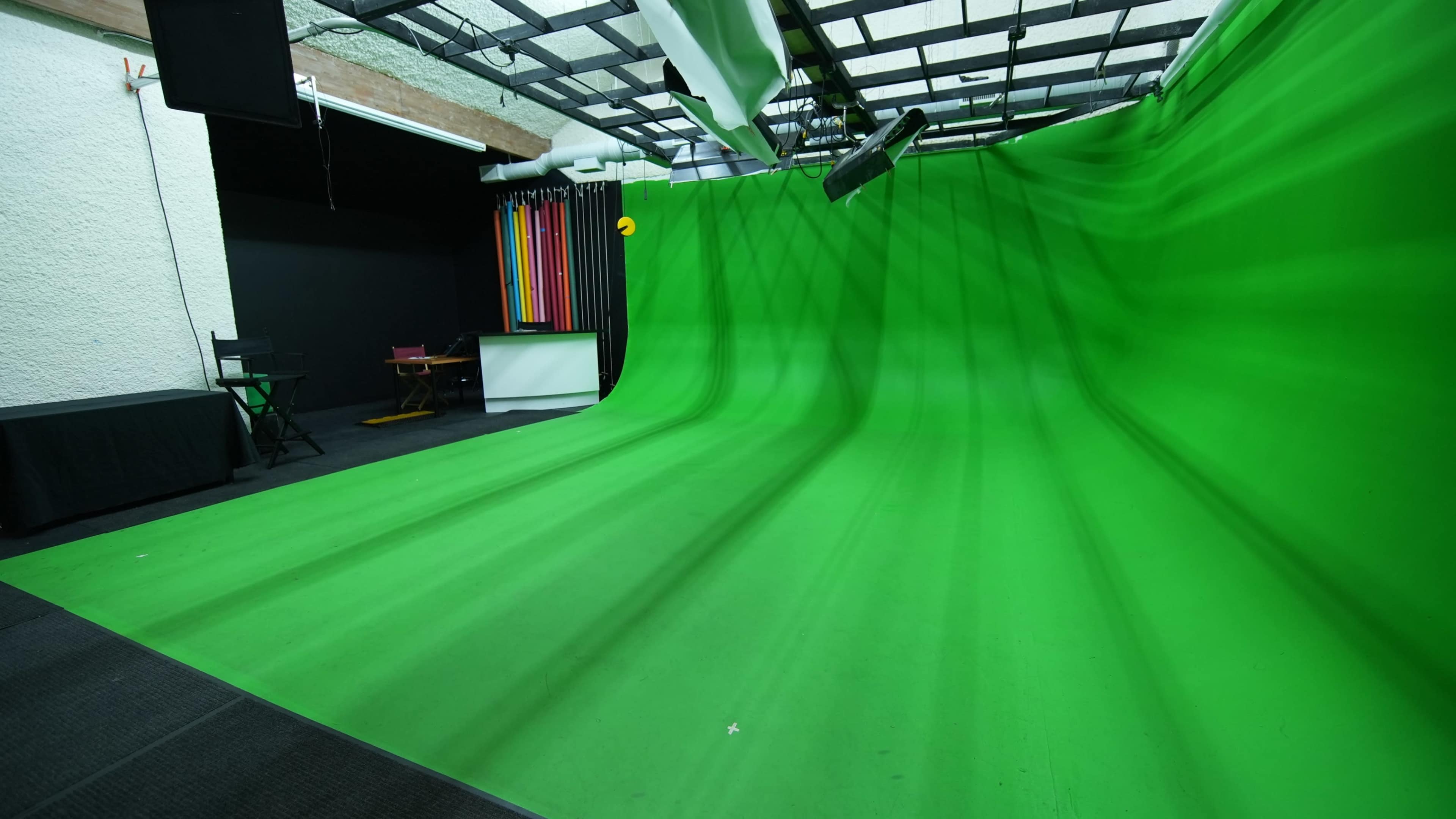 The image shows a green screen studio with a smooth green backdrop and various colored backgrounds in the background.