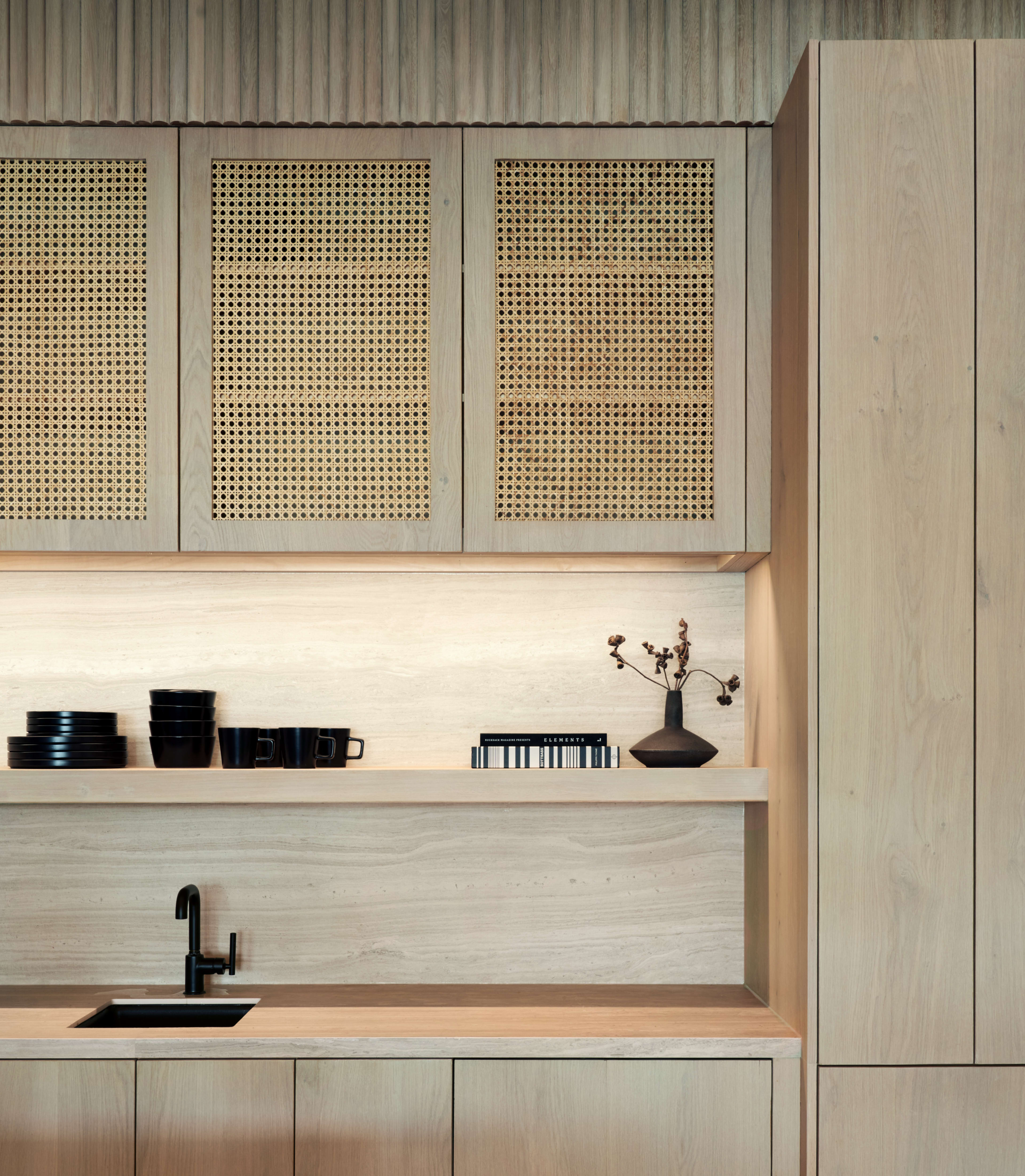A modern kitchen featuring wooden cabinetry, open shelving with black dishware, and a sink with a black faucet.