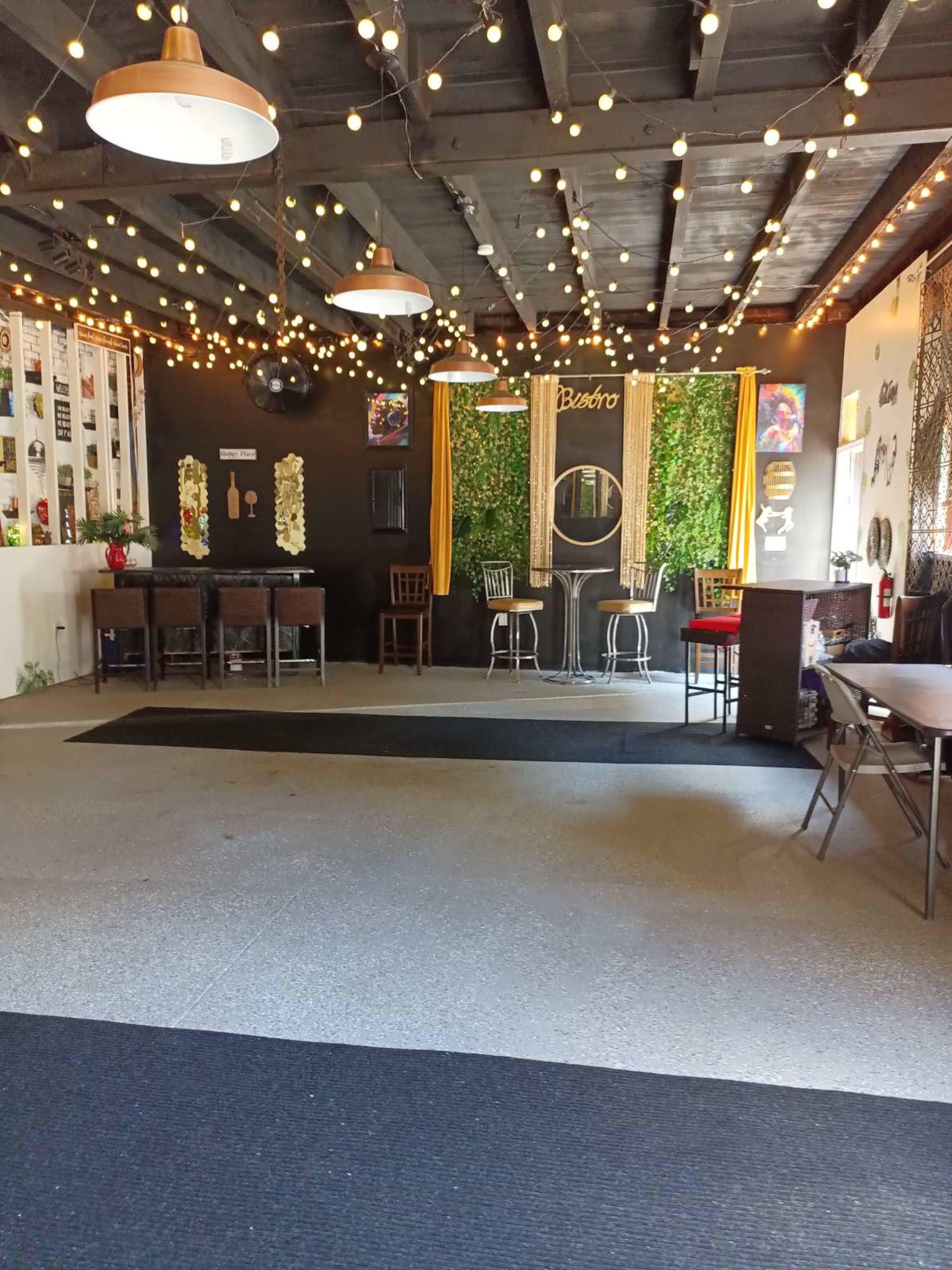 The image shows an interior space decorated with string lights, featuring a bar area with chairs and a green wall accent.