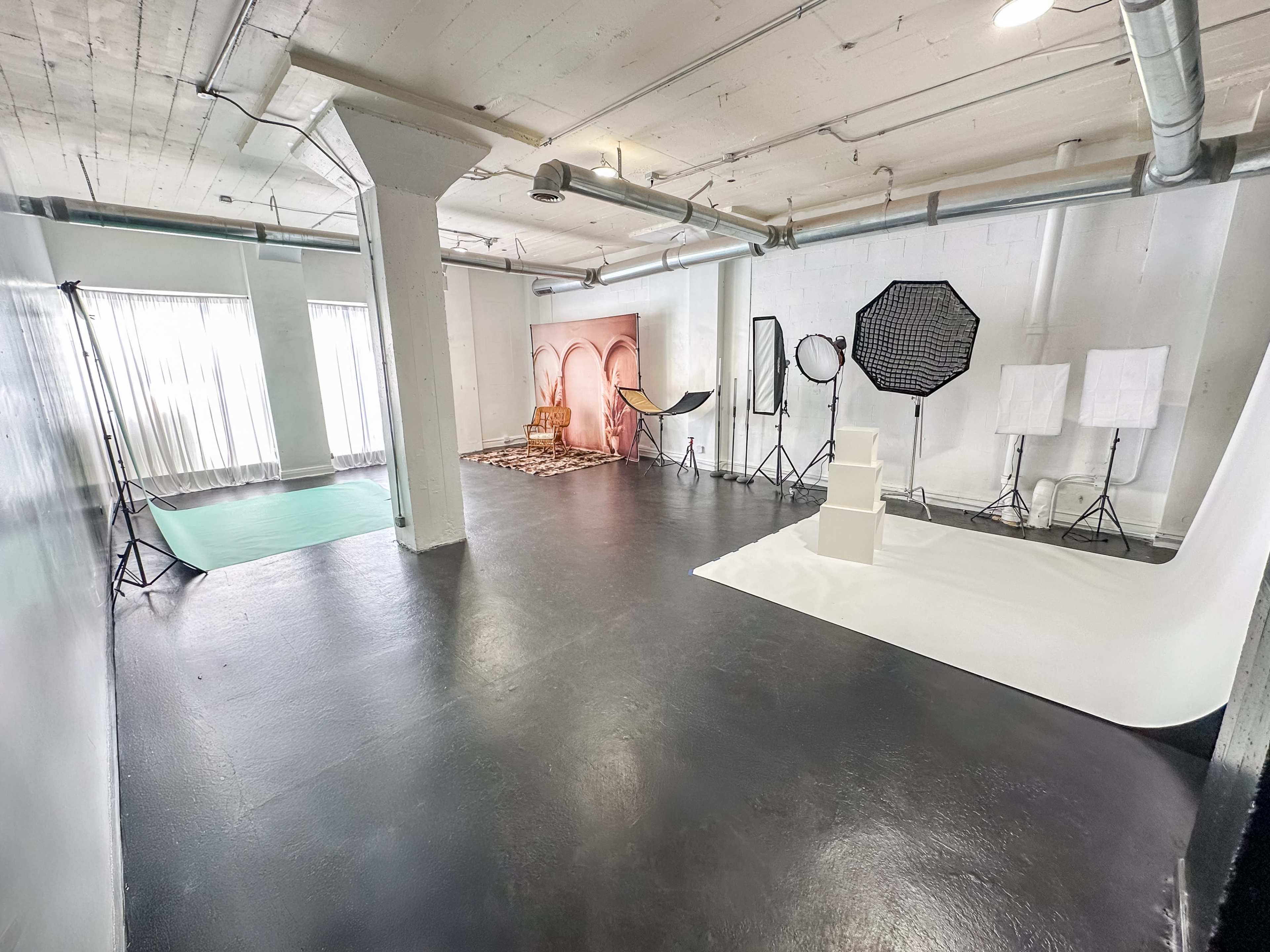 The image shows a spacious photography studio with various backdrops, lighting equipment, and a clean black floor.