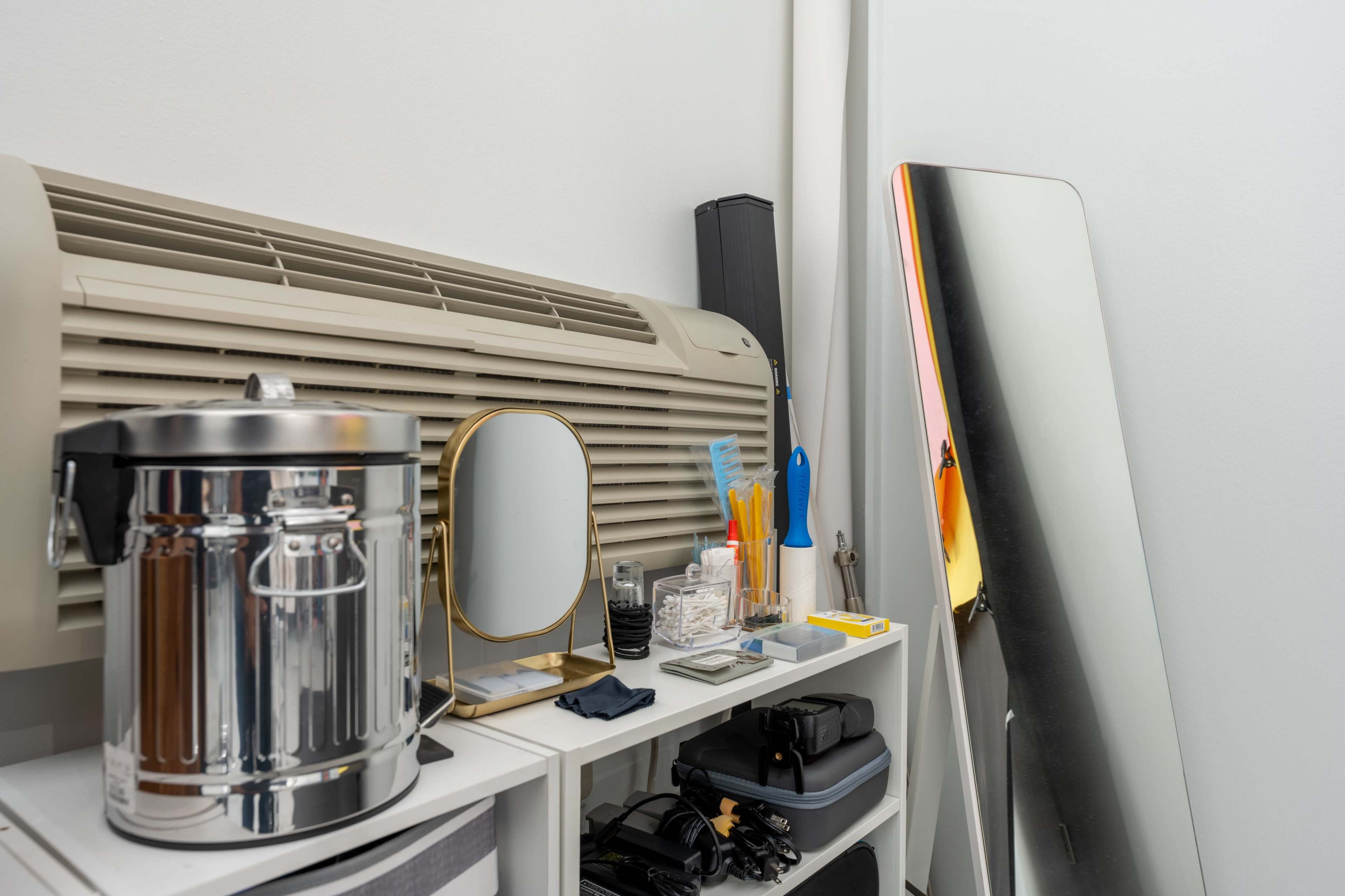 A collection of organizational items, including a mirror, a metal container, and various tools, is arranged on a shelf beside an air conditioning unit.