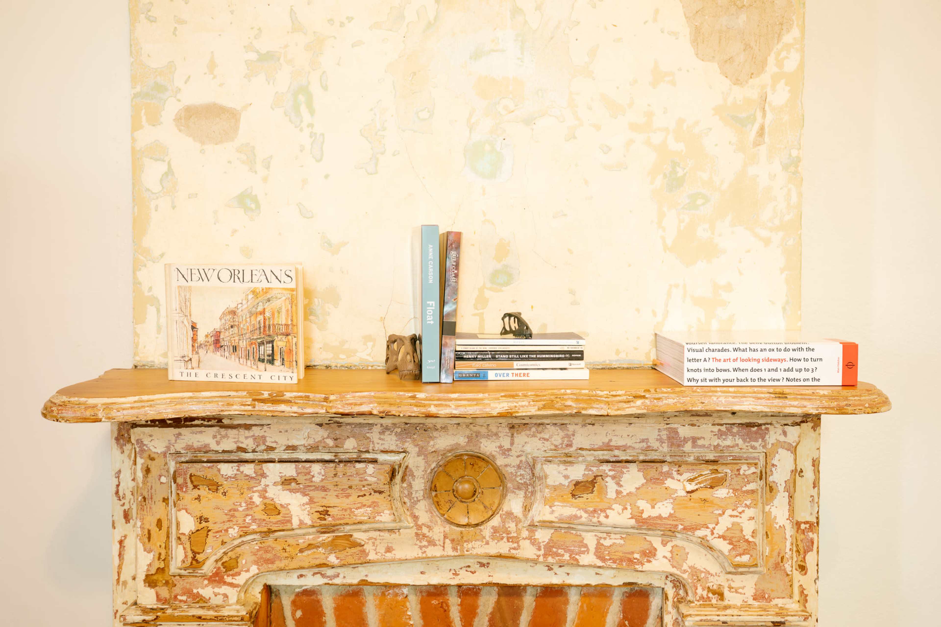 A weathered mantelpiece displays a book about New Orleans alongside several other books and small decorative items.