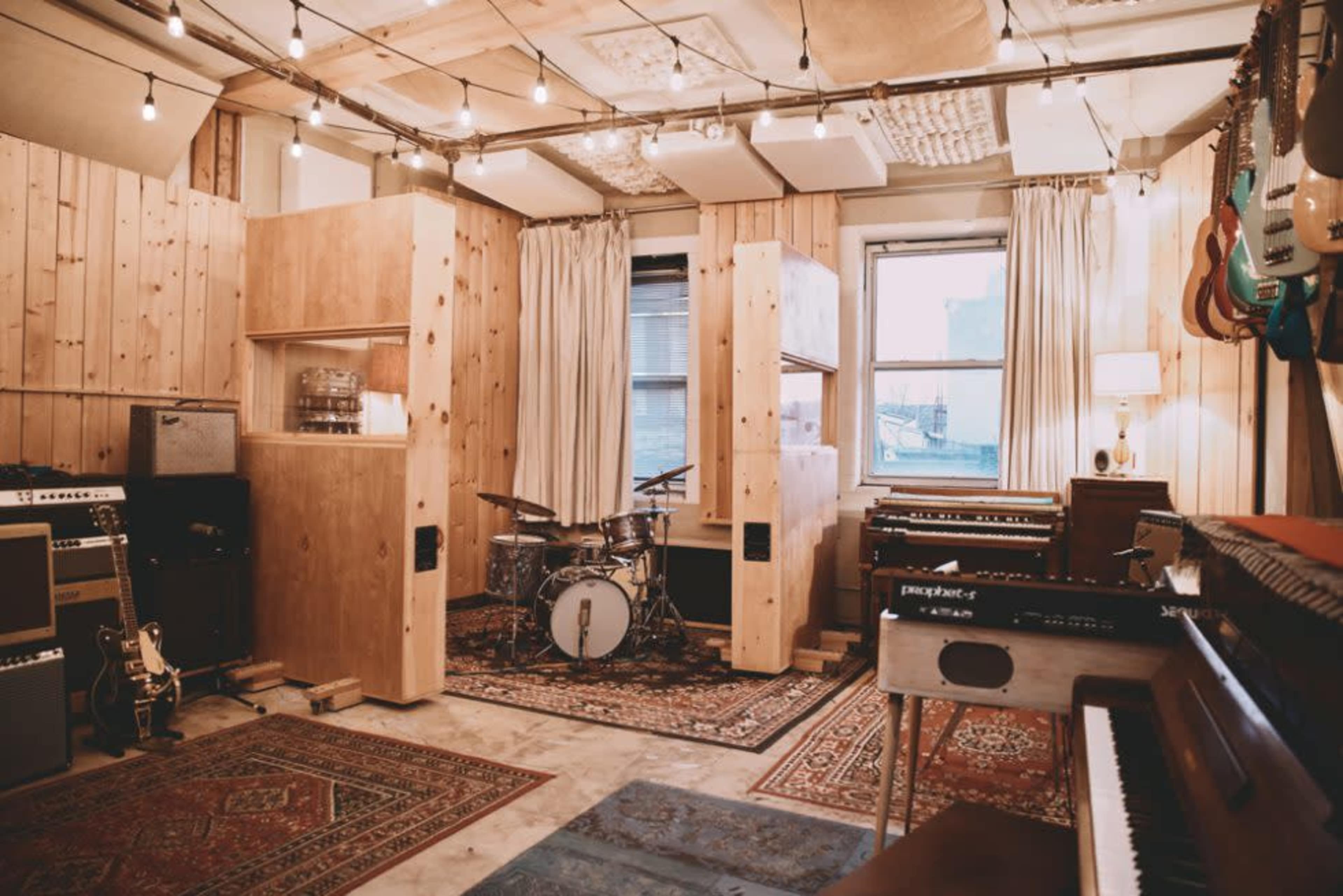 A cozy music studio with wooden walls, a drum set, various musical instruments, and warm lighting.