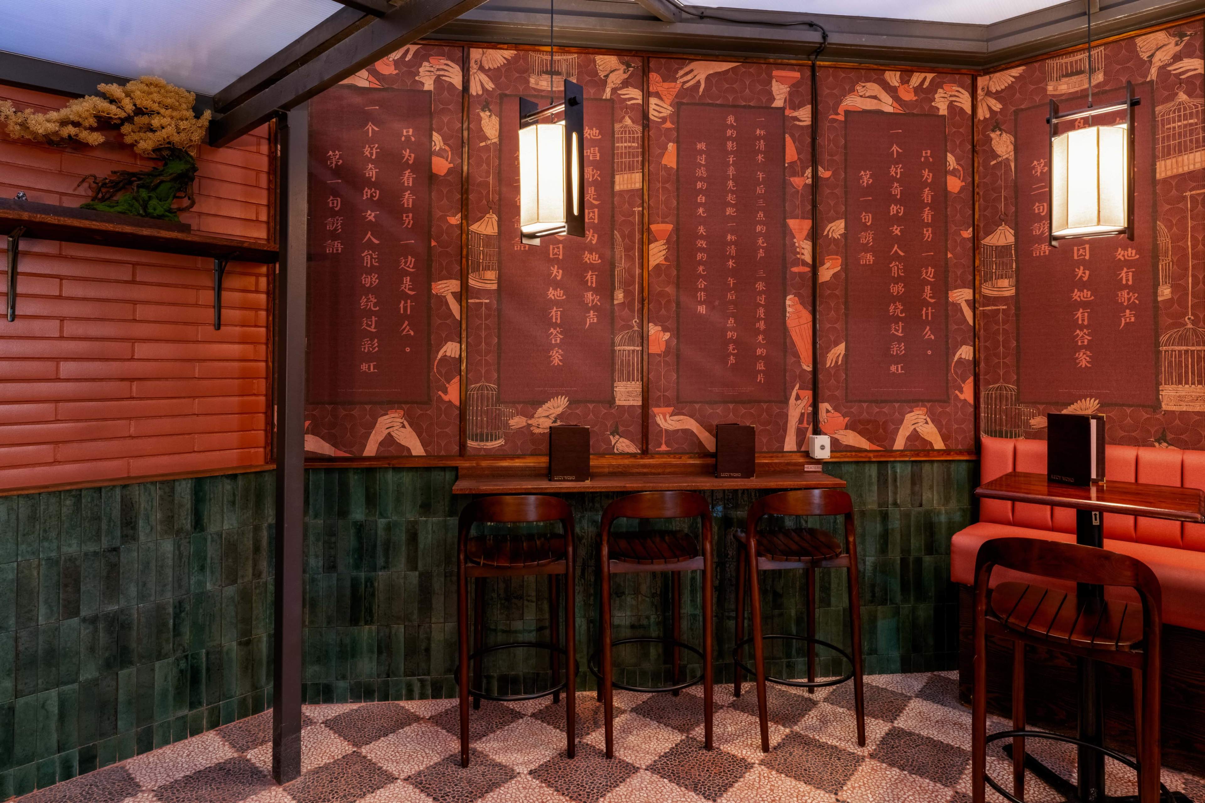 The image shows a cozy corner of a restaurant featuring patterned wallpaper, a wooden table, and high stools.