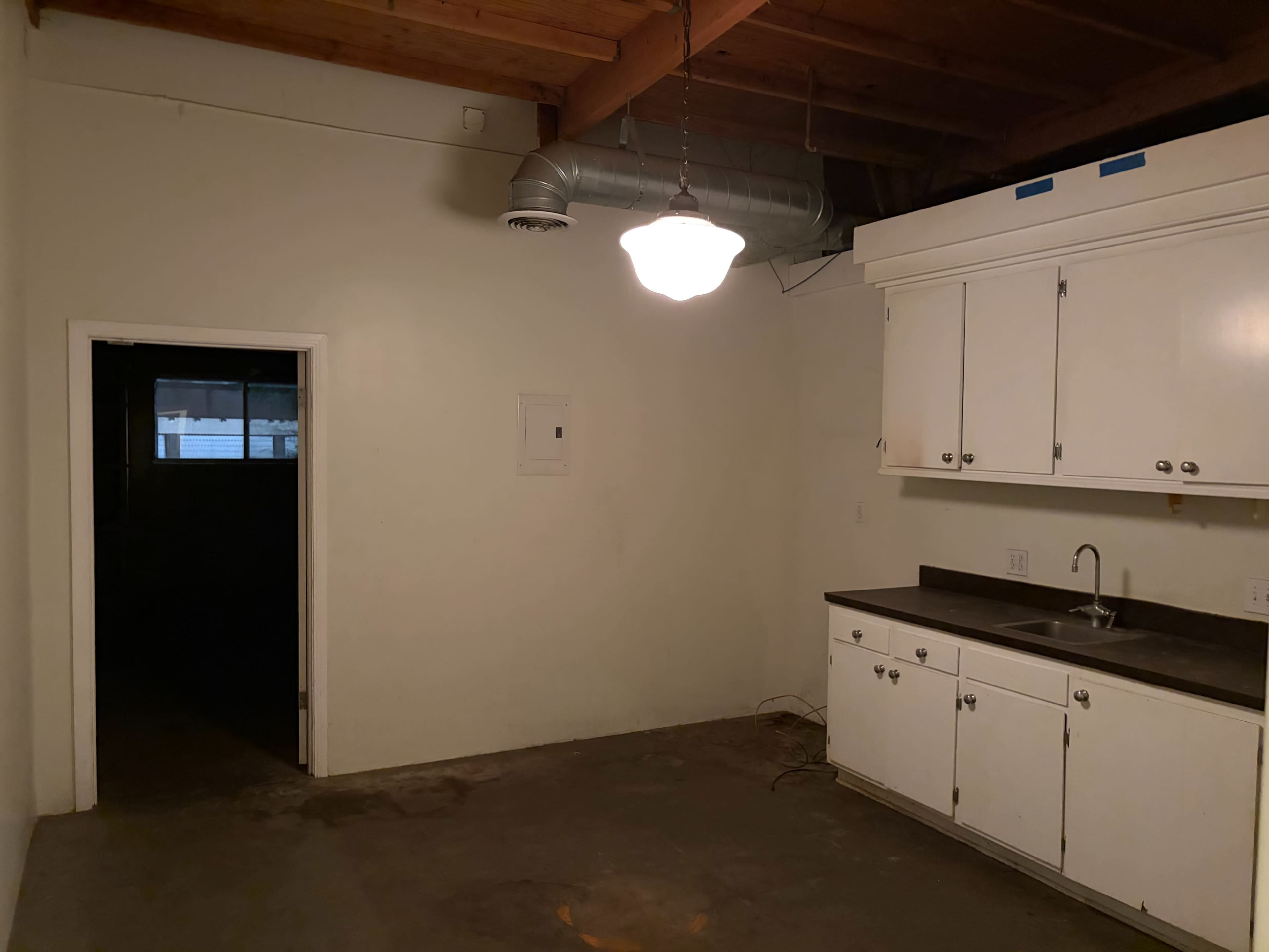 The image shows a simple kitchen area with white cabinets, a sink, and a doorway leading to another room.