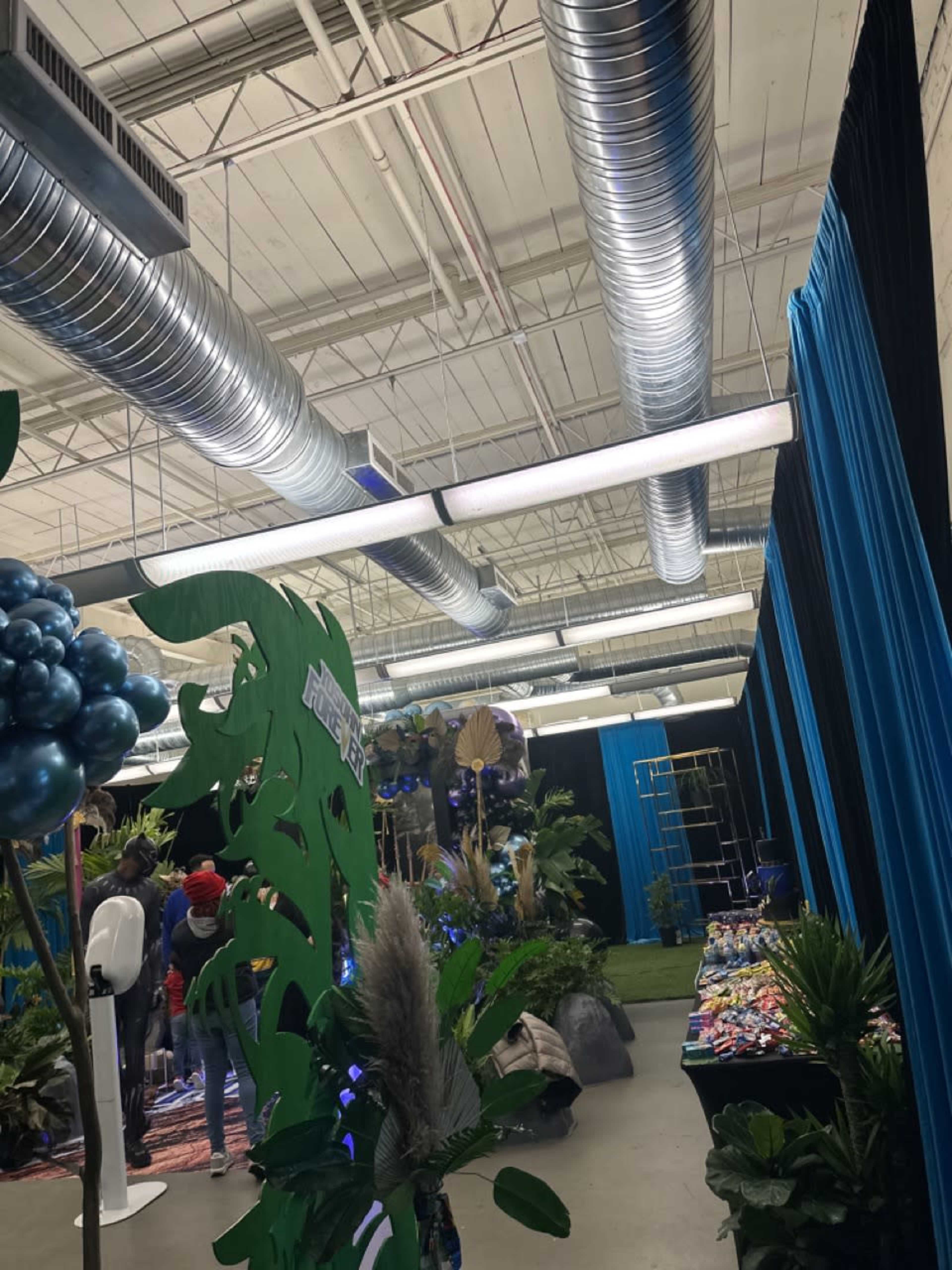 An indoor event space with blue curtains, decorative plants, and metallic ventilation ducts overhead.