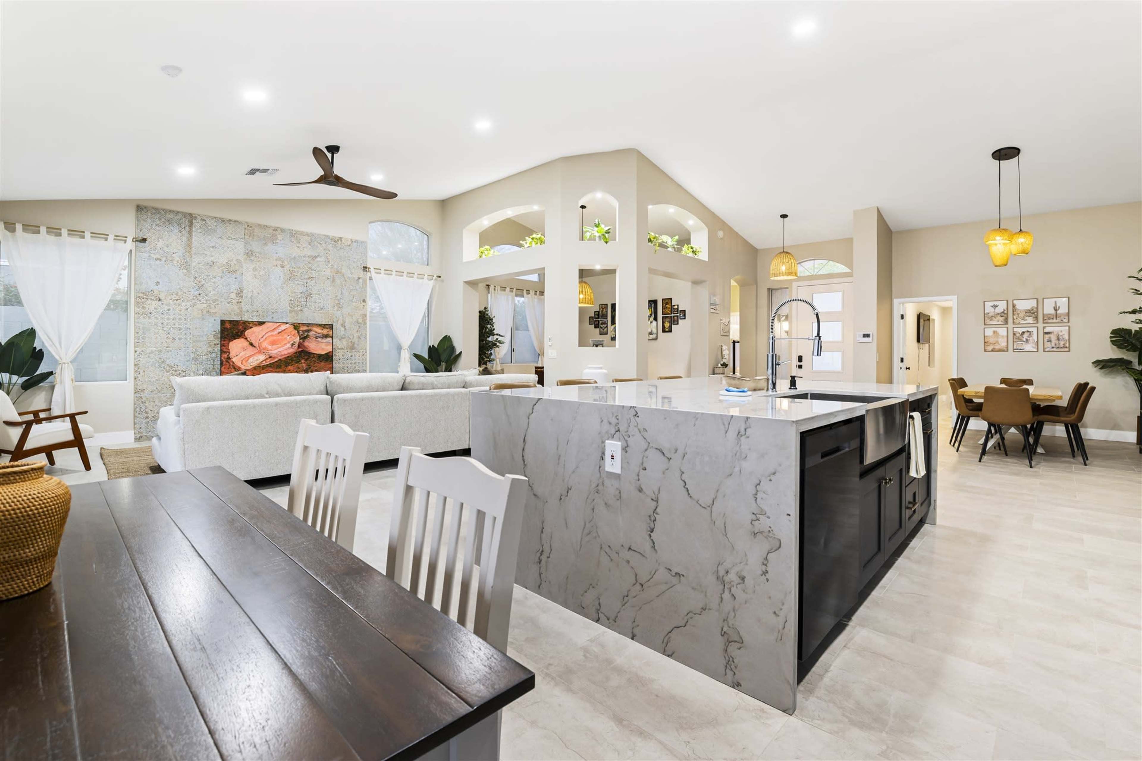 A modern open-concept living space featuring a kitchen island, a dining area, and a cozy seating area with a large window.