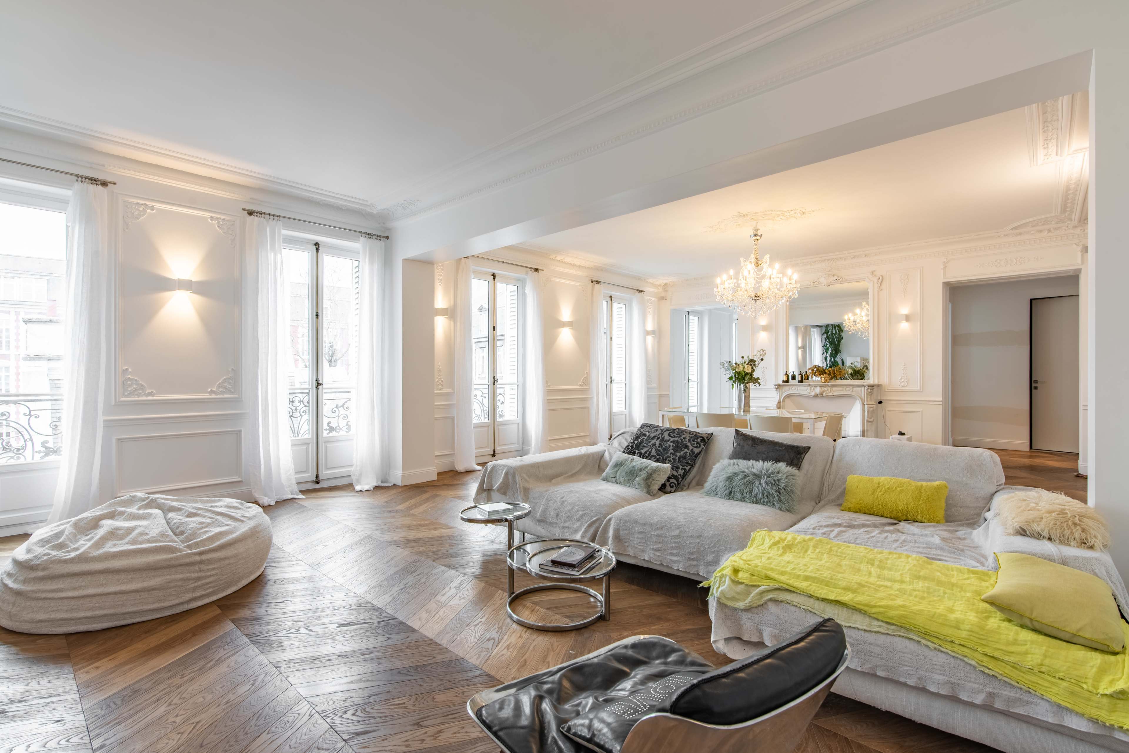 A spacious, elegantly furnished living room with large windows, hardwood floors, and a mix of modern and soft seating arrangements.