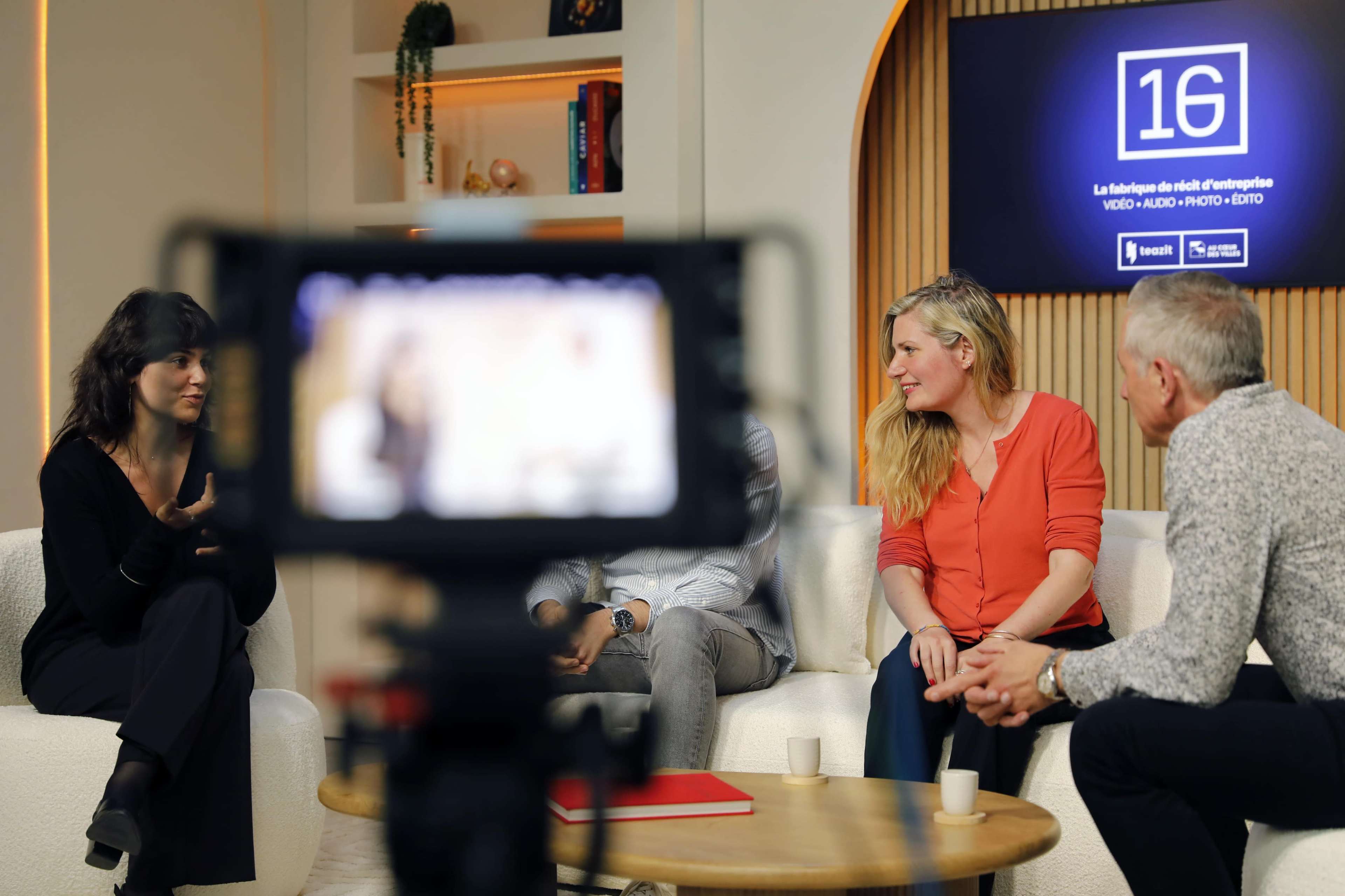 A group of four people engage in conversation during a recorded discussion in a studio setting.