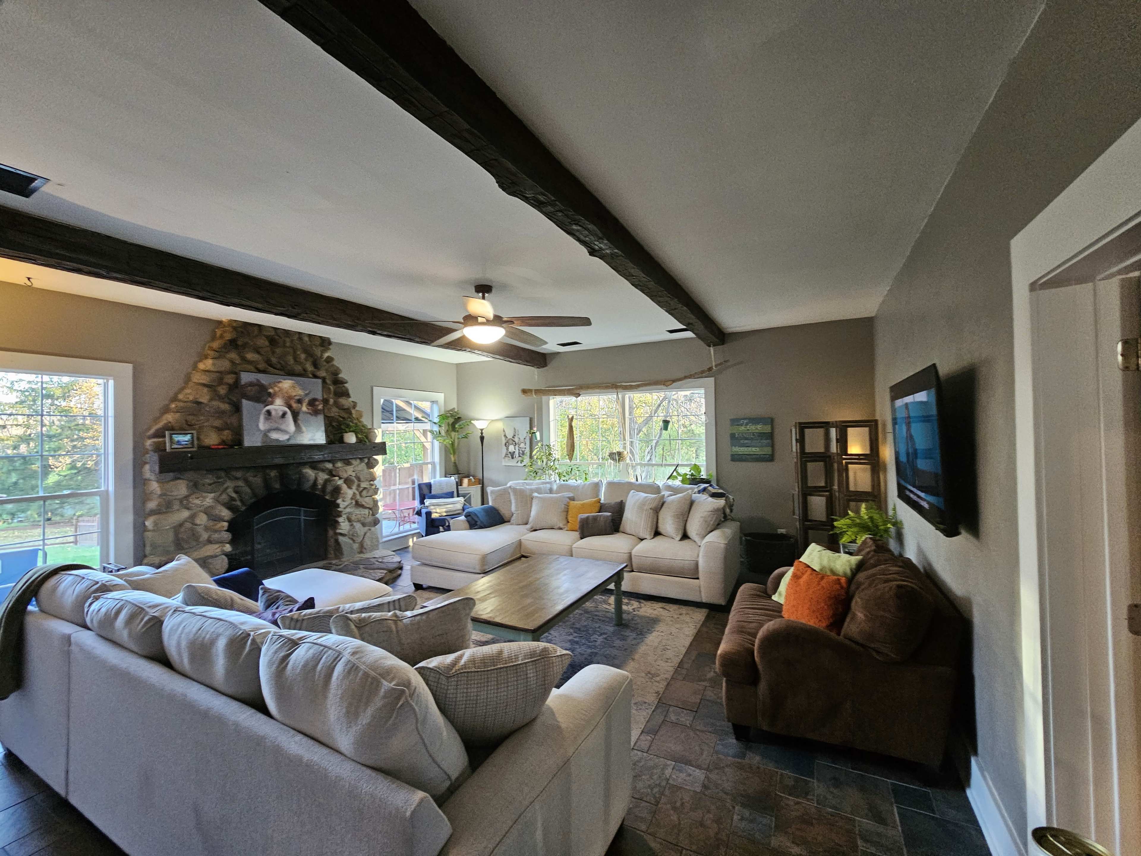 The living room features a stone fireplace, multiple seating areas with light-colored sofas, and large windows that overlook a garden.