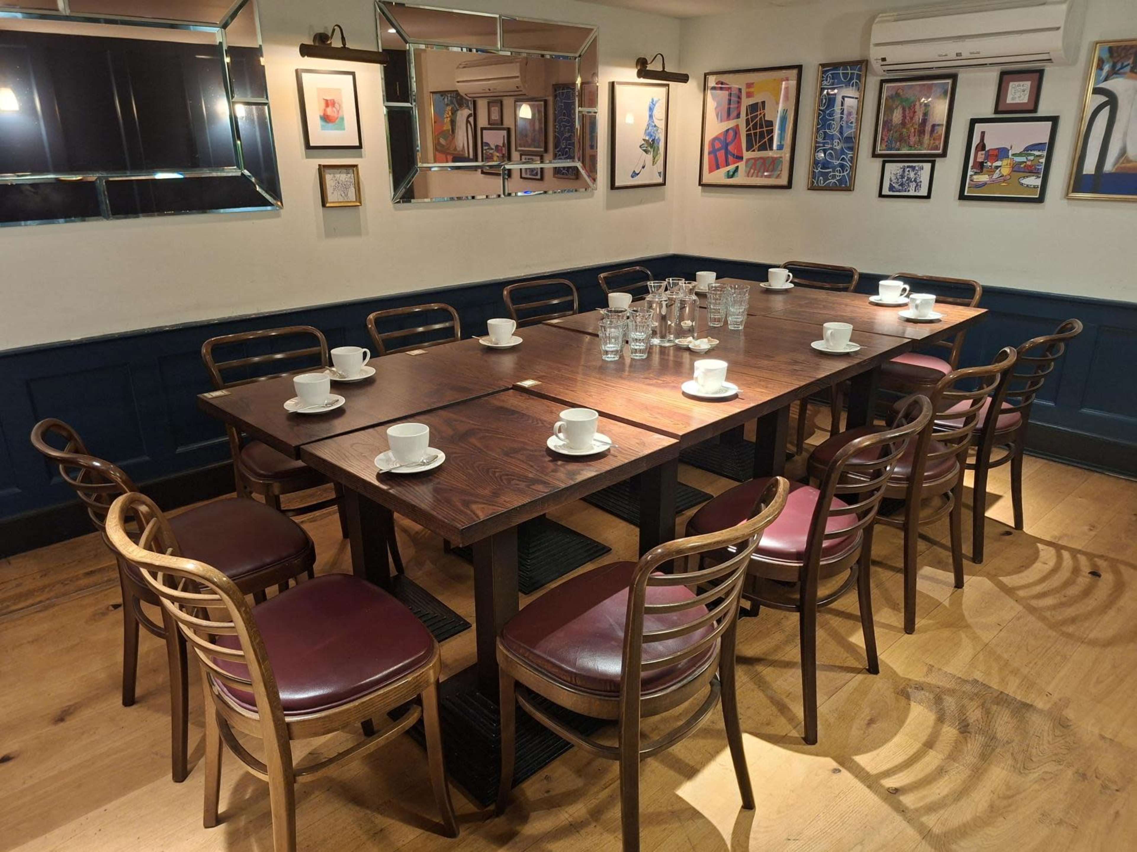 A large wooden dining table is set with white cups and surrounded by wooden chairs in a well-decorated room featuring various artworks on the walls.