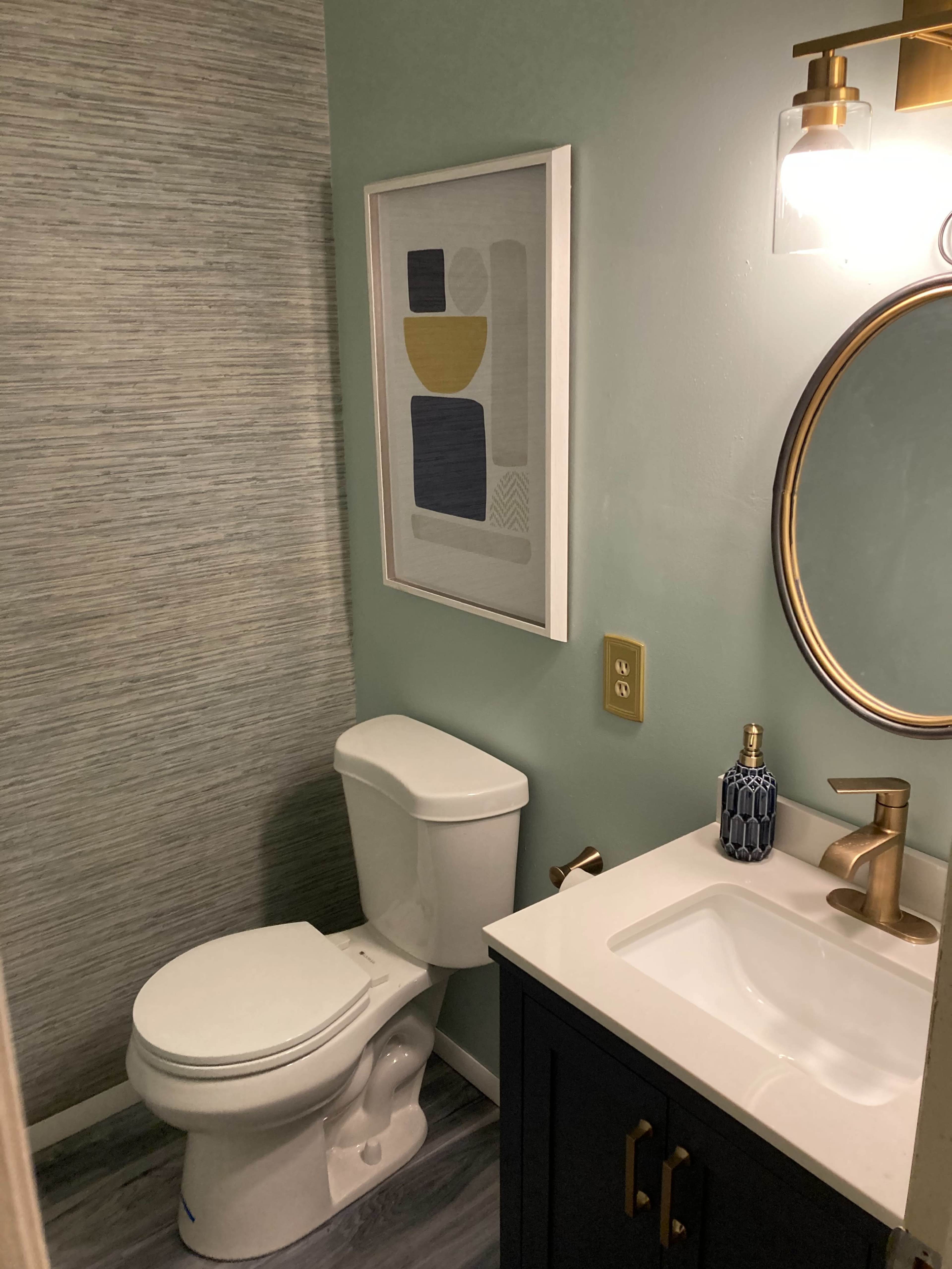 A small bathroom featuring a white toilet, a dark vanity with a sink, and a framed abstract artwork on the wall.