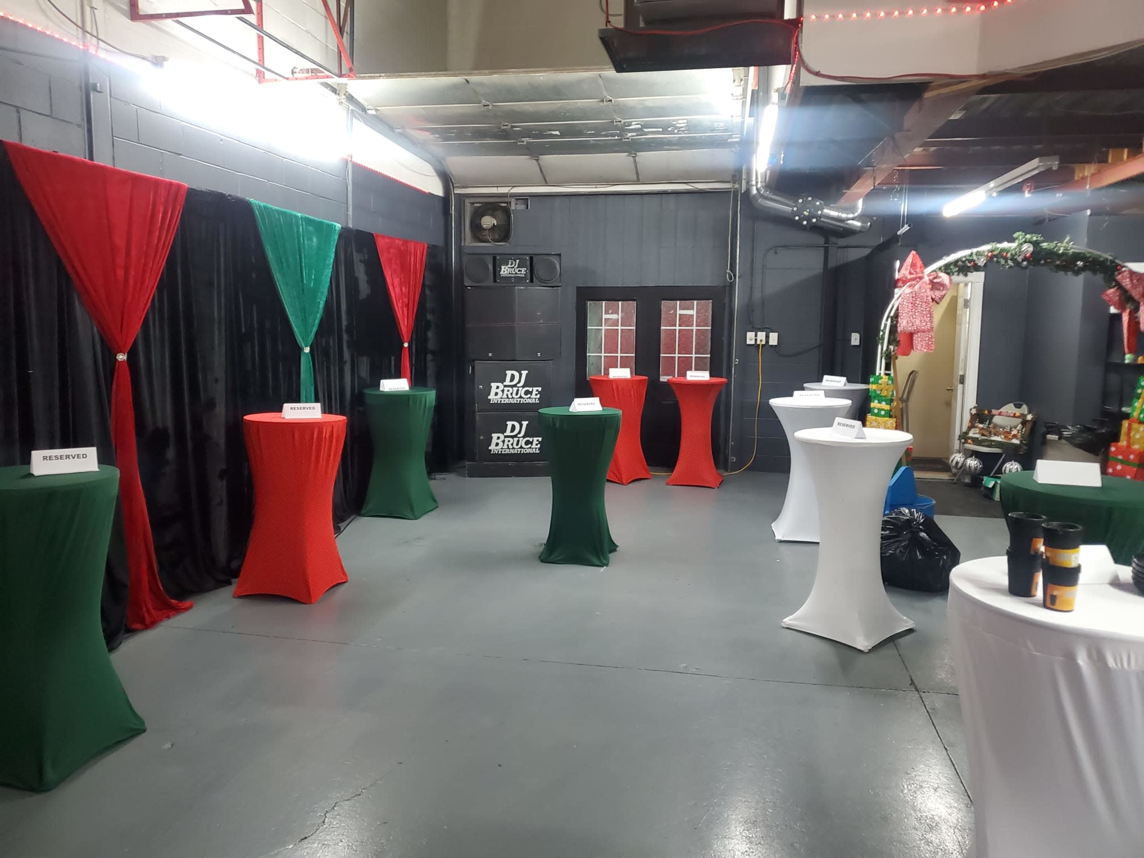 The room features several tall tables covered with white, red, and green cloths, with black and colorful fabric drapes along the walls.