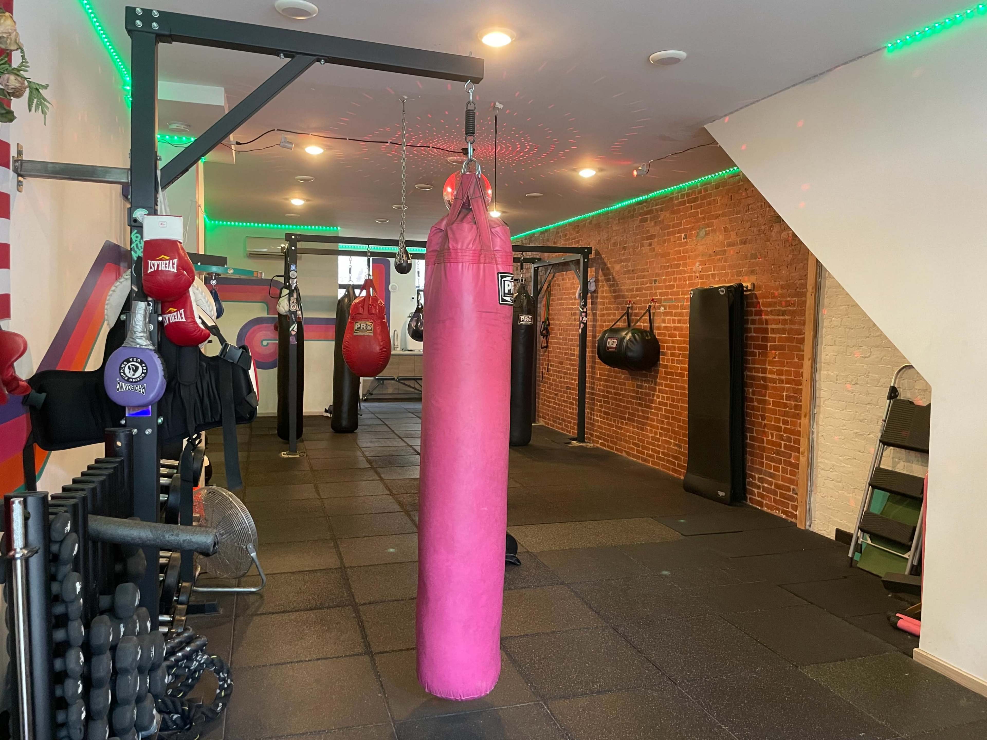 A fitness gym with various punching bags, exercise equipment, and a pink heavy bag hanging in the center.