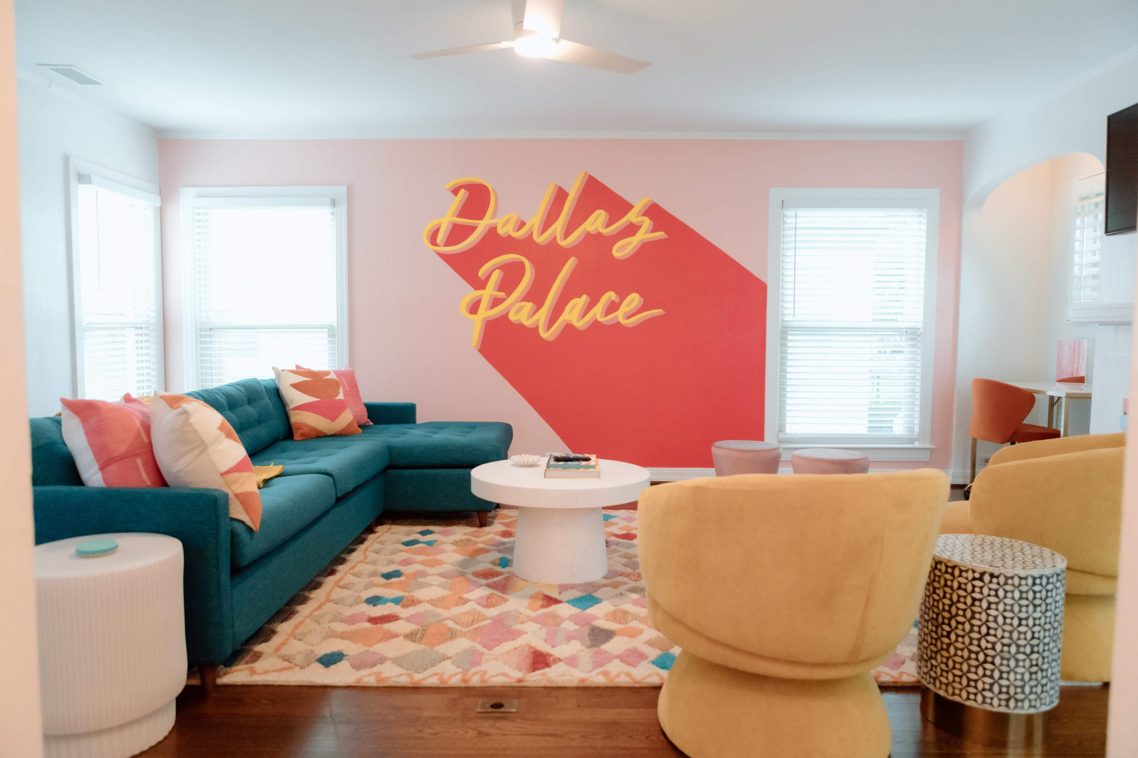 A brightly colored living room with a blue sectional sofa, a round coffee table, and a large wall featuring the text "Dallas Palace."
