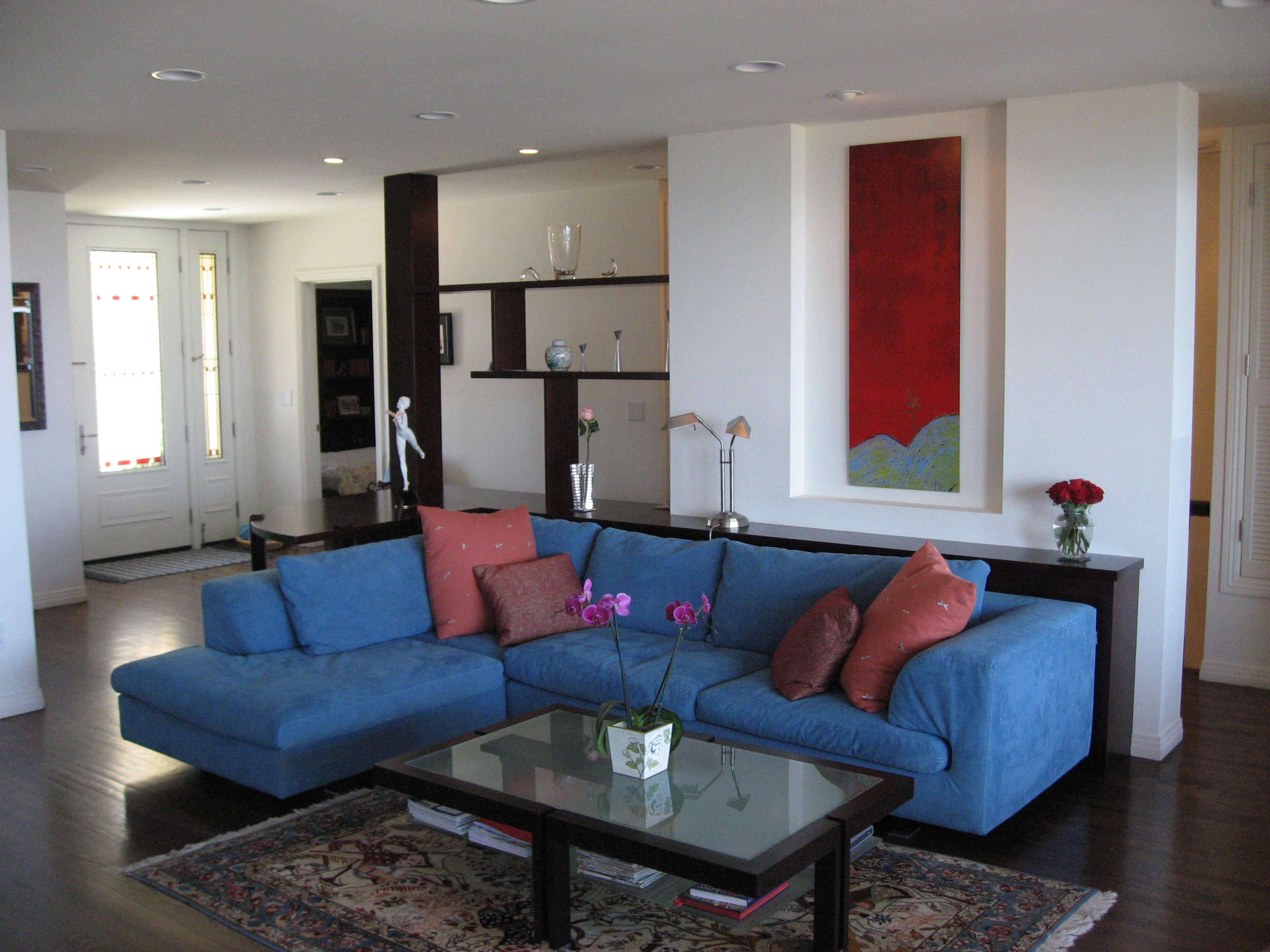 A modern living room featuring a blue sectional couch, a glass coffee table, and a red abstract painting on the wall.