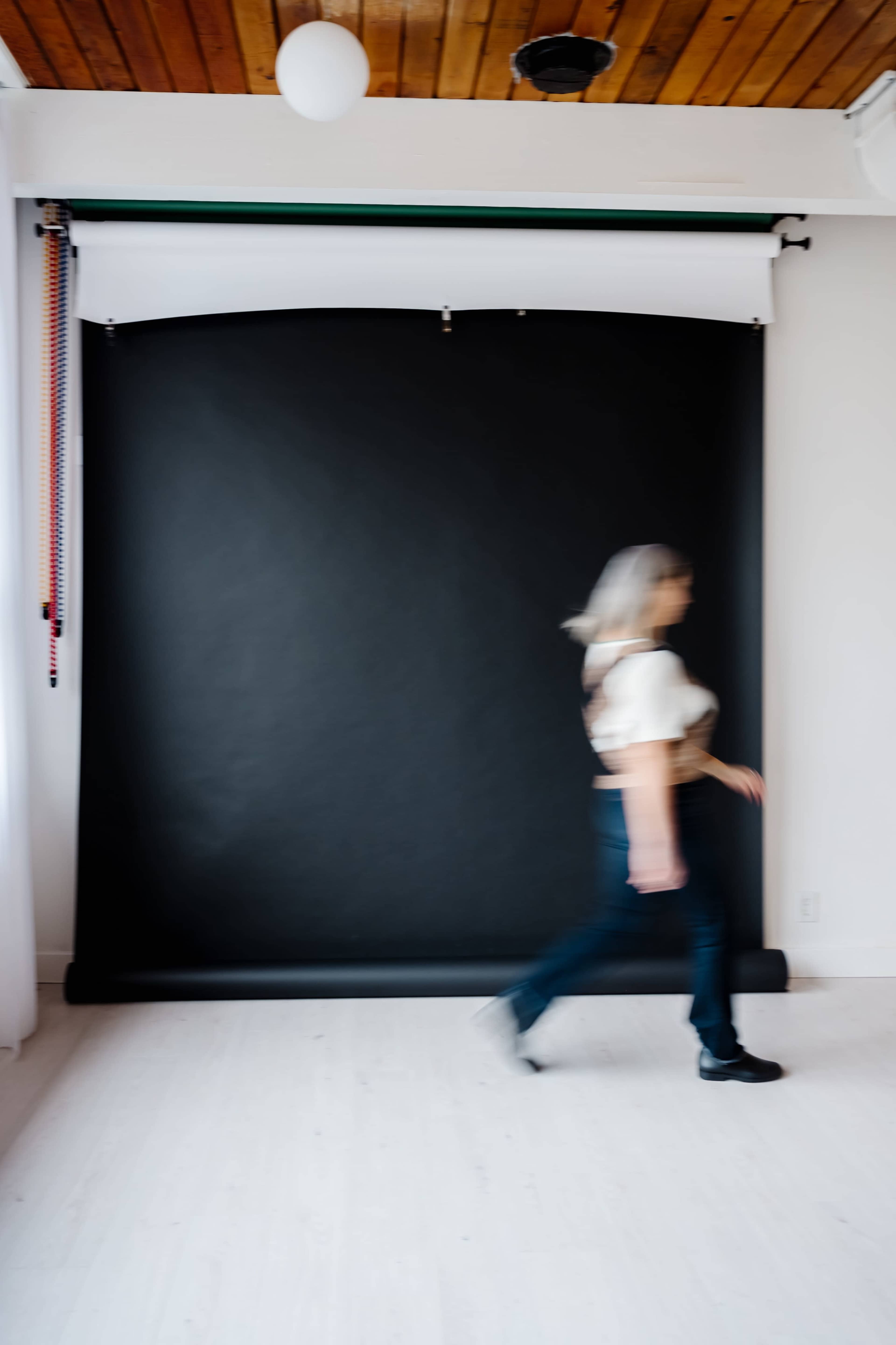 A person walks past a black photography backdrop in a bright studio space.