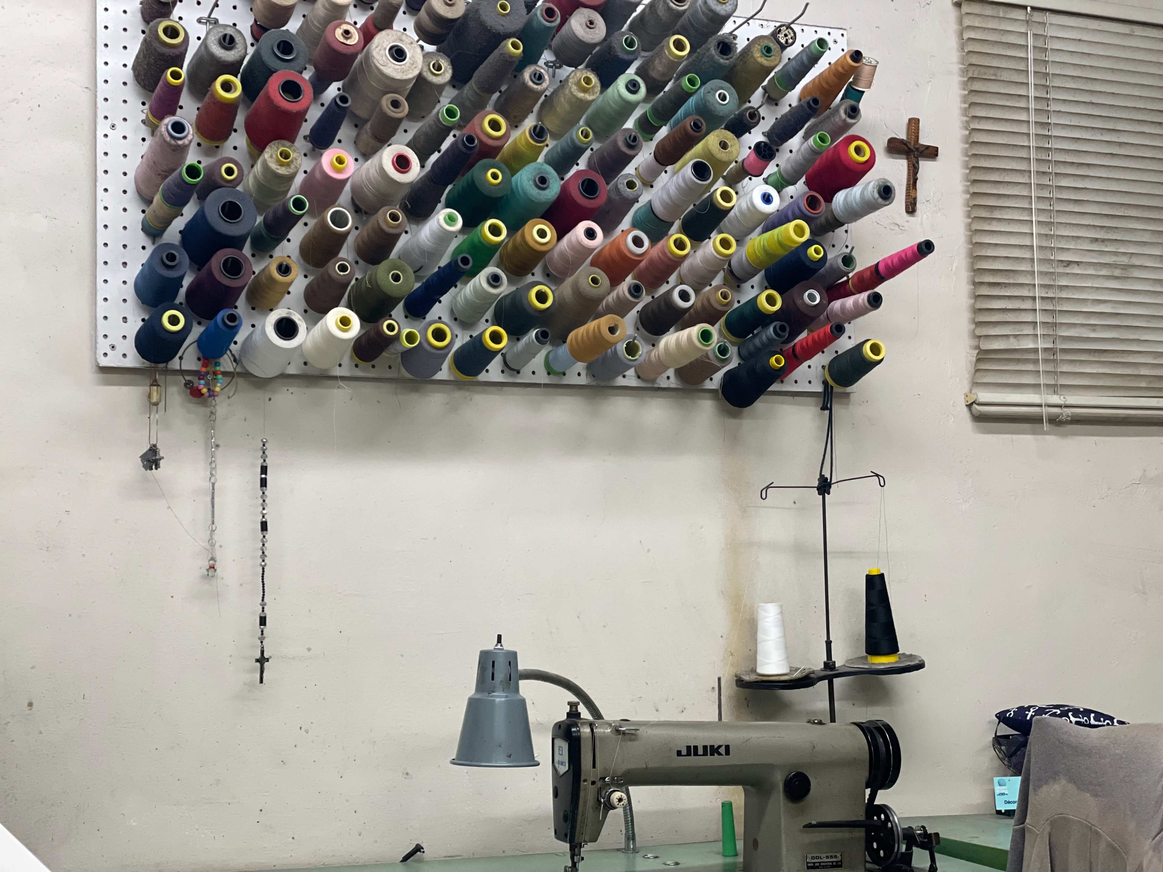 A sewing machine sits on a table beneath a wall-mounted panel displaying an array of colorful spools of thread.