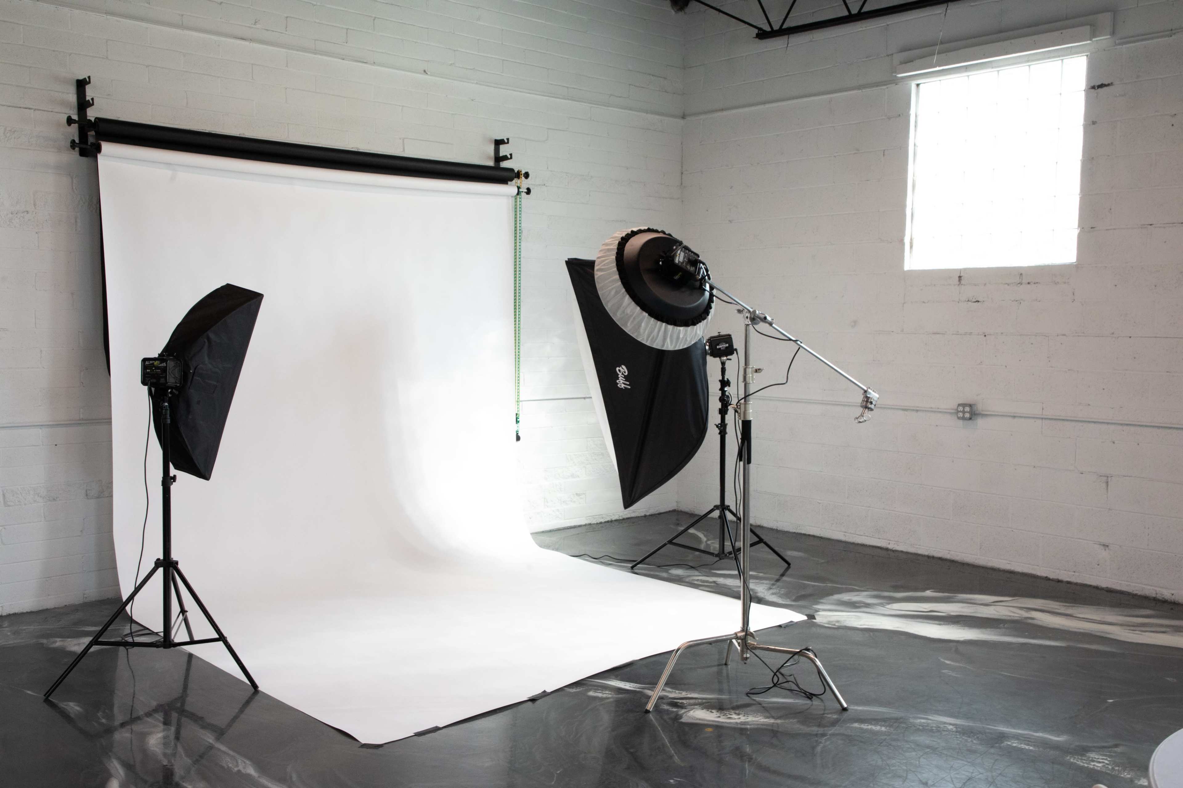 A photography studio setup with a white backdrop, two softbox lights on stands, and a large light modifier.