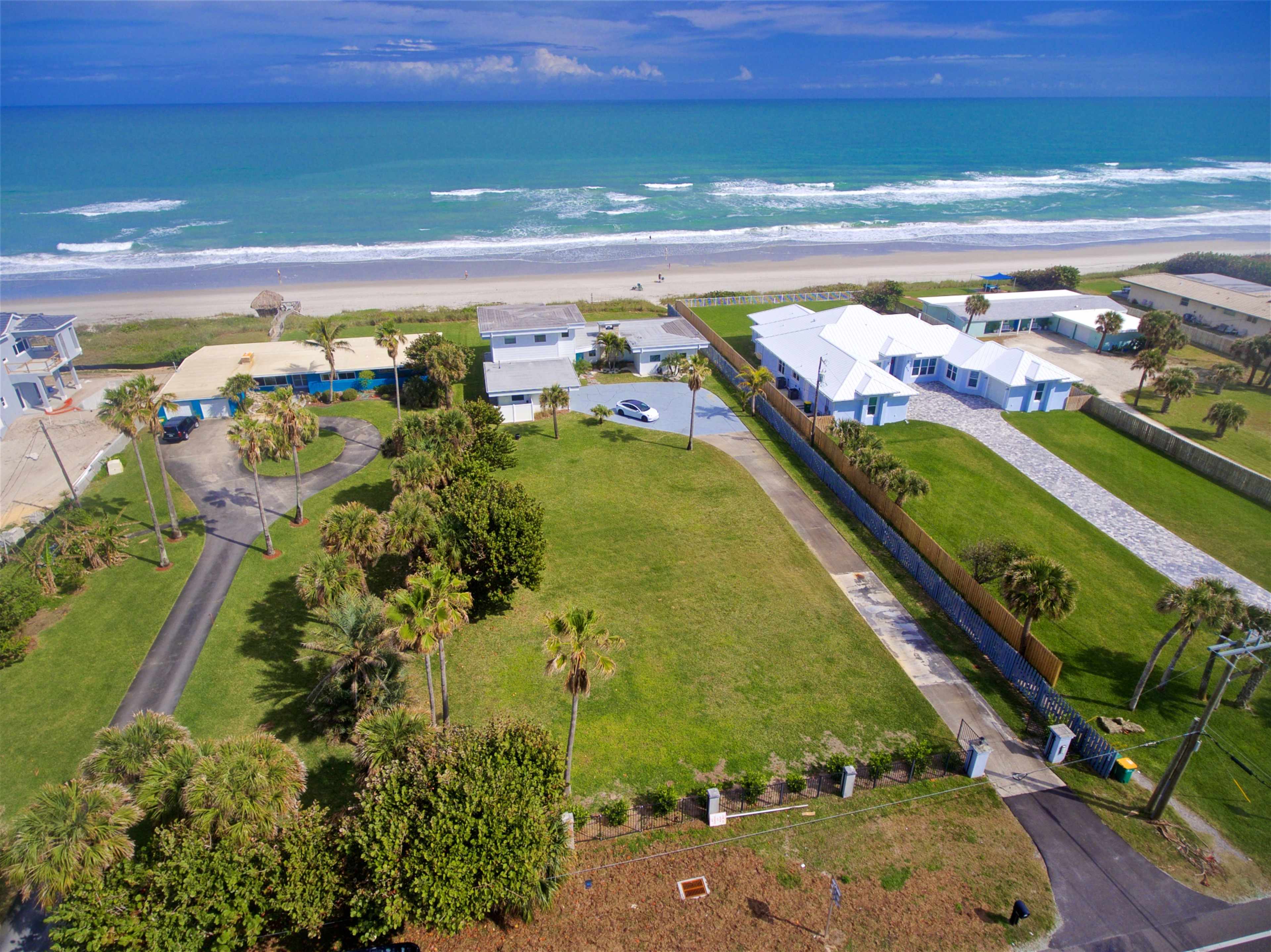 A coastal property with several houses, palm trees, and a stretch of sandy beach along a turquoise ocean.