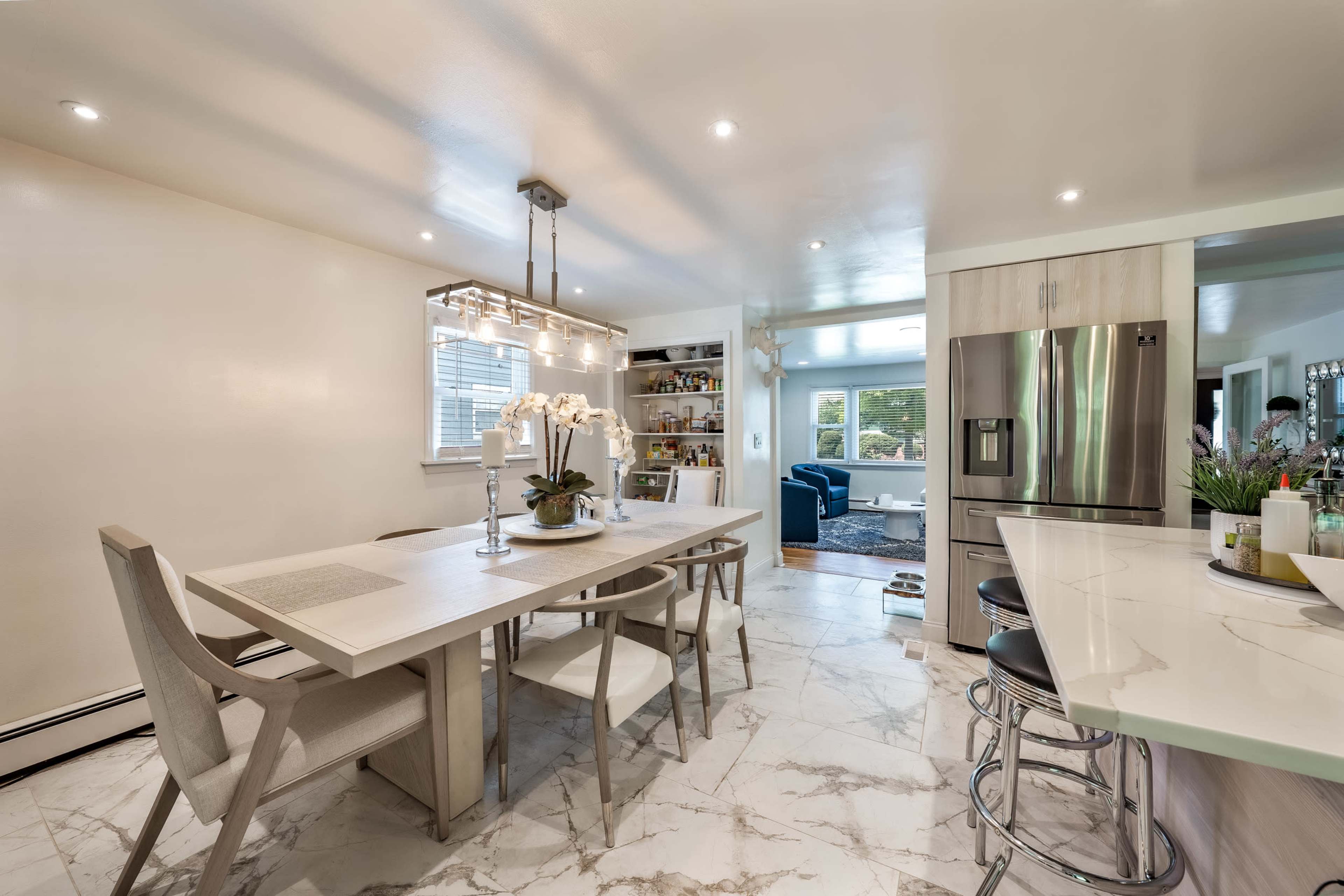A modern kitchen features a dining table, marble flooring, and a view into a connected living space.