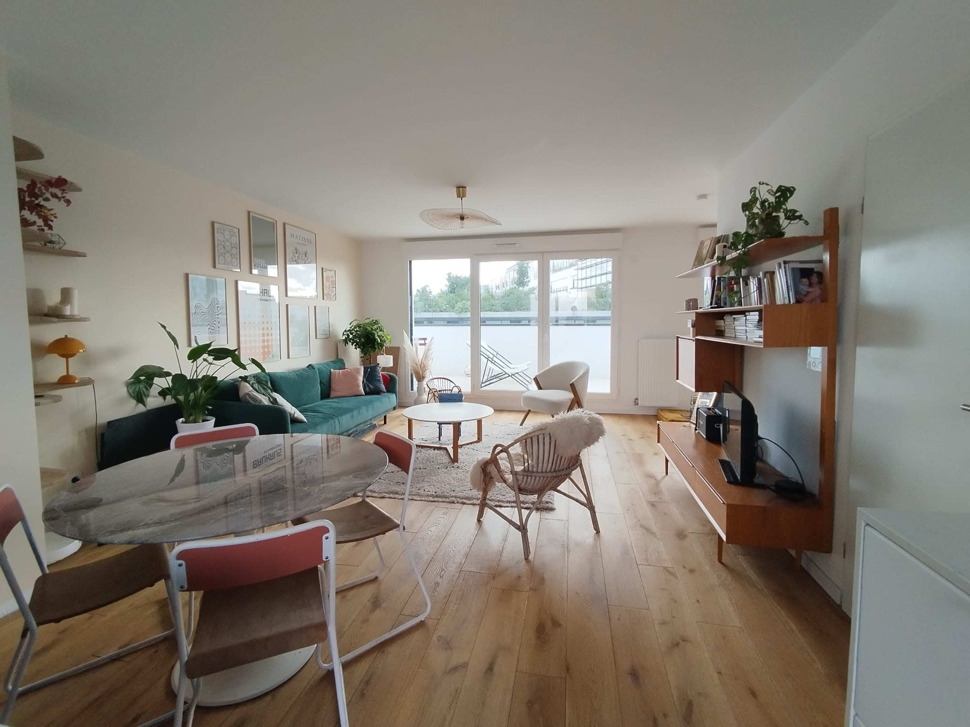 A spacious living room with a green sofa, a round coffee table, and large windows that open to a balcony.