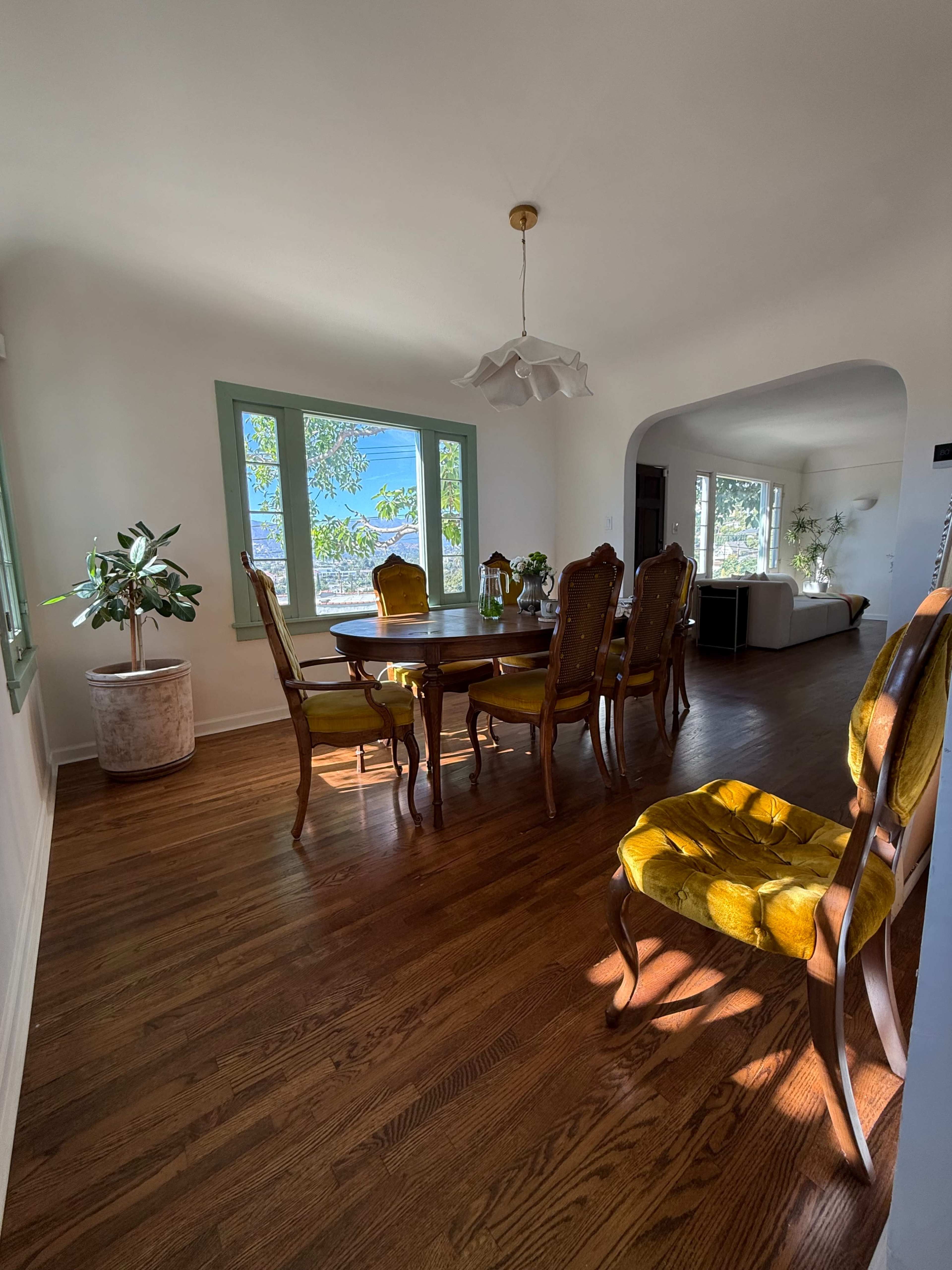 A dining room features a wooden table surrounded by six ornate chairs, with large windows allowing natural light to fill the space.