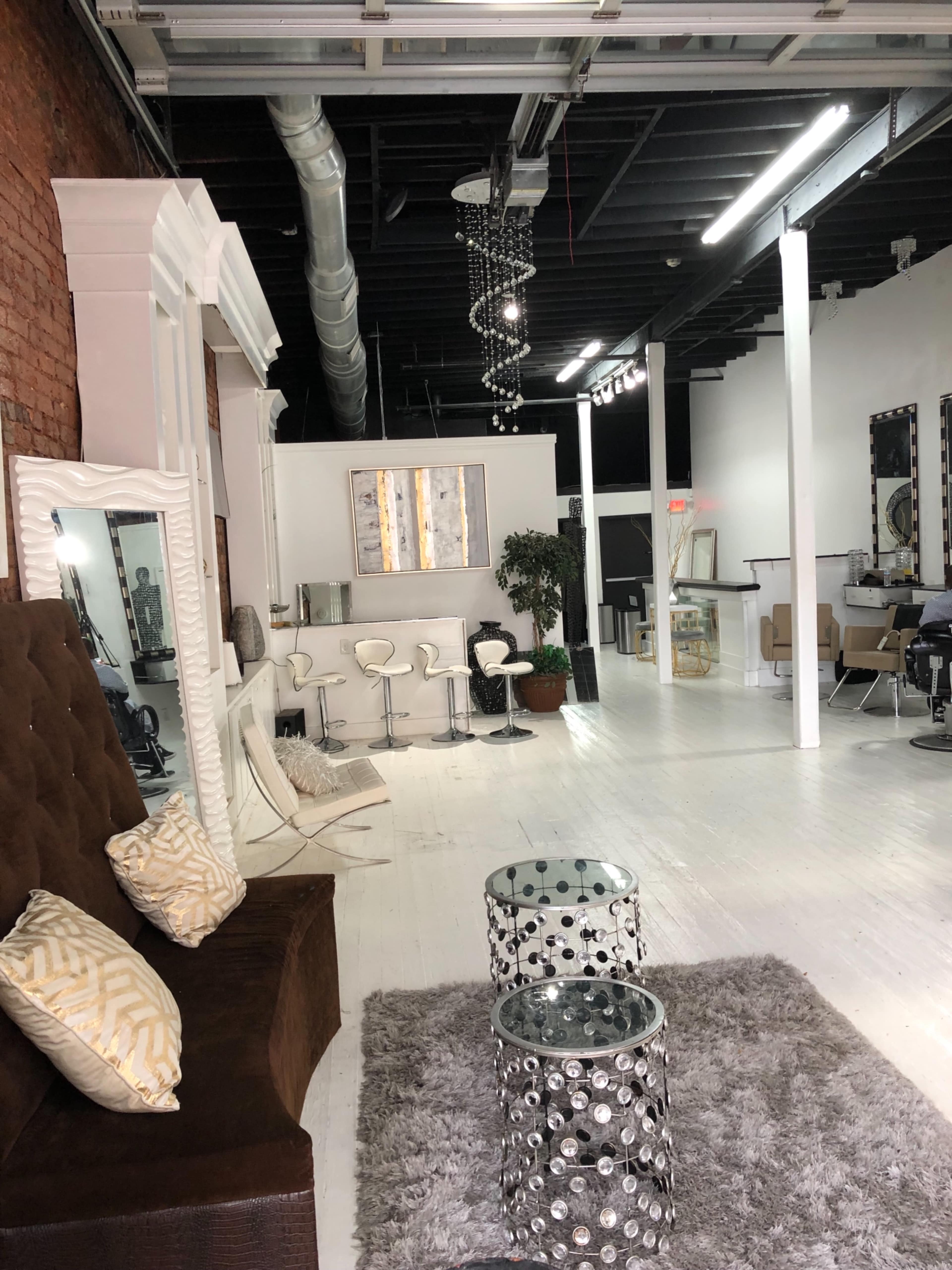 The image depicts a modern interior of a salon or lounge with stylish seating, a decorative mirror, mirrored coffee tables, and a bright, spacious environment.