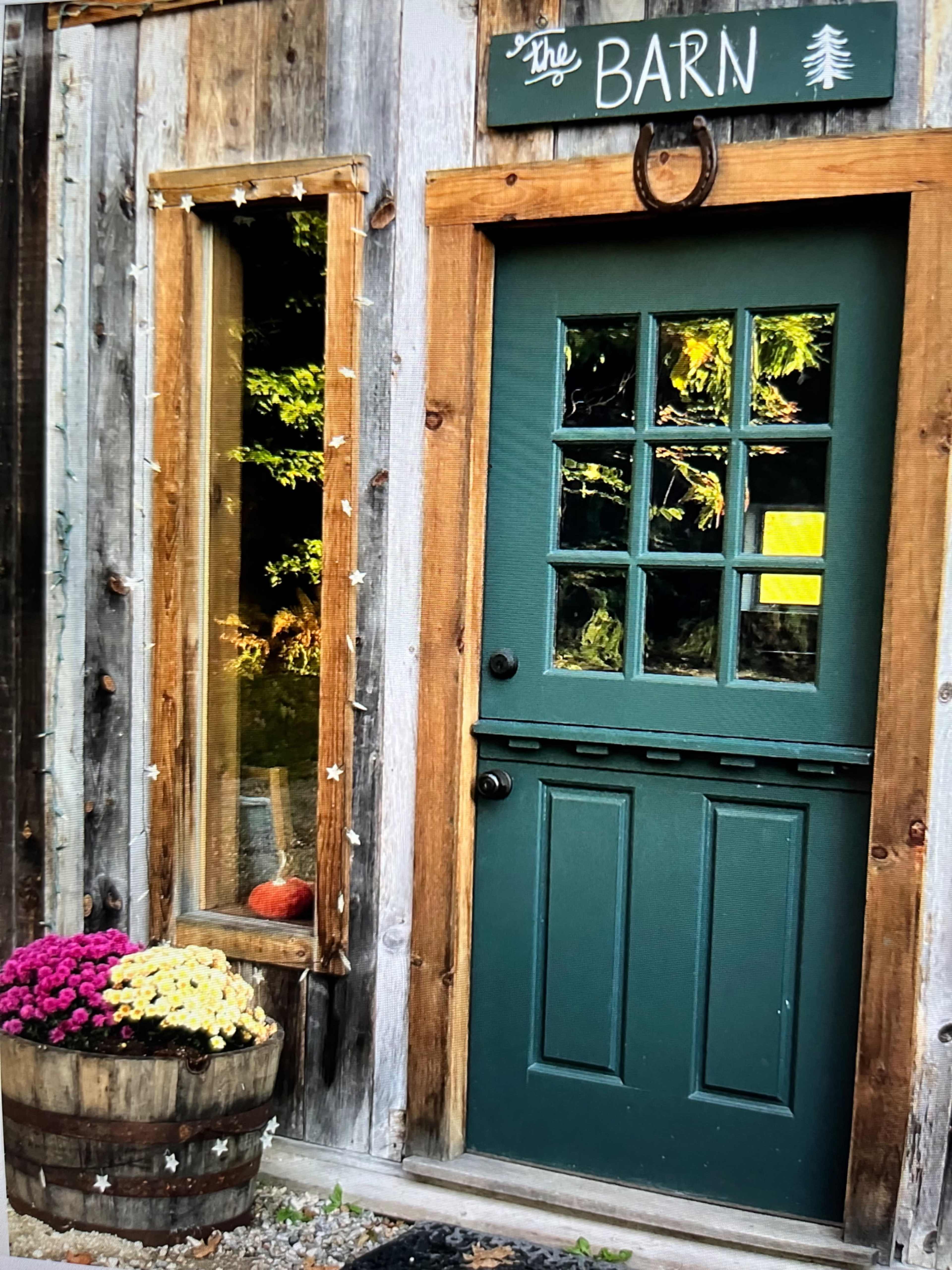 A wooden barn door with a window beside it, decorated with flowers in a barrel at its base.