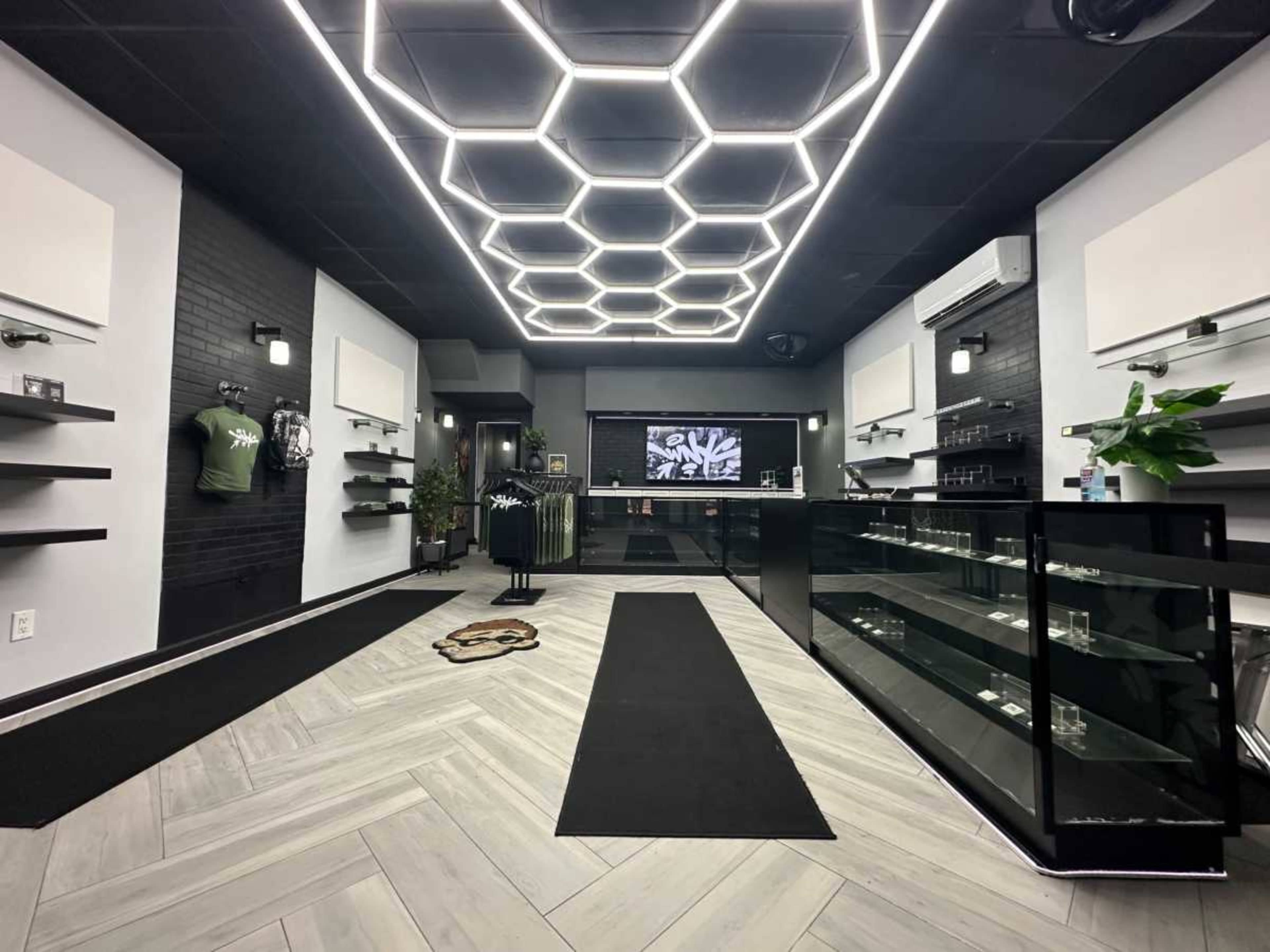 The image shows a modern retail space with a hexagonal light fixture, sleek glass display cases, and minimalistic shelving against dark walls.