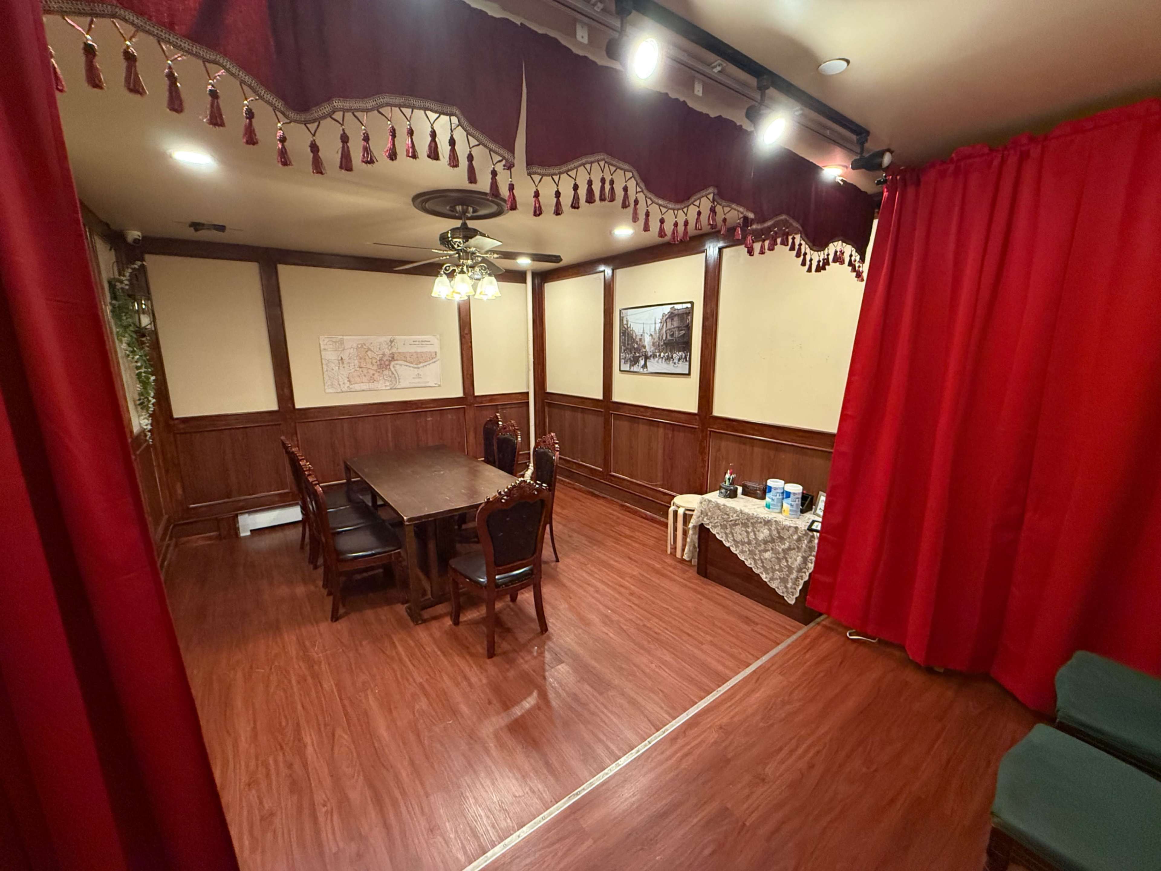 The image shows a wood-paneled room with a large dining table, chairs, and red curtains hanging along the walls.