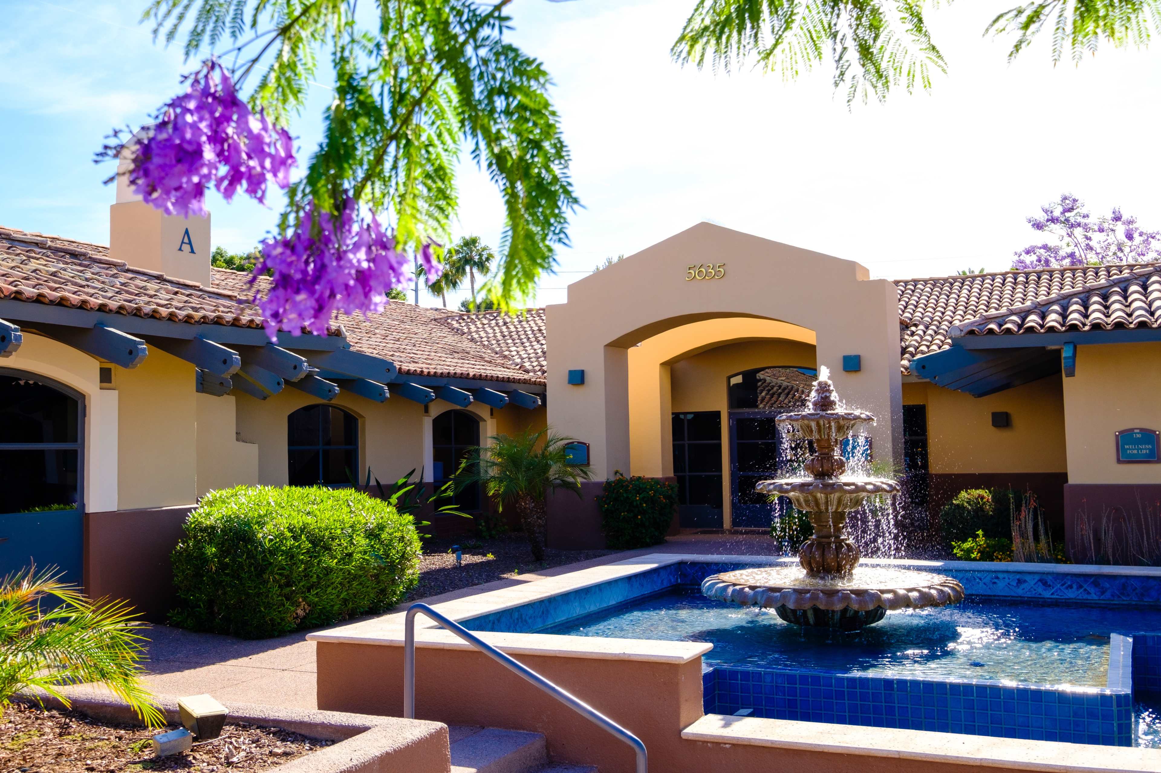 A building with a fountain surrounded by lush landscaping and blooming flowers.