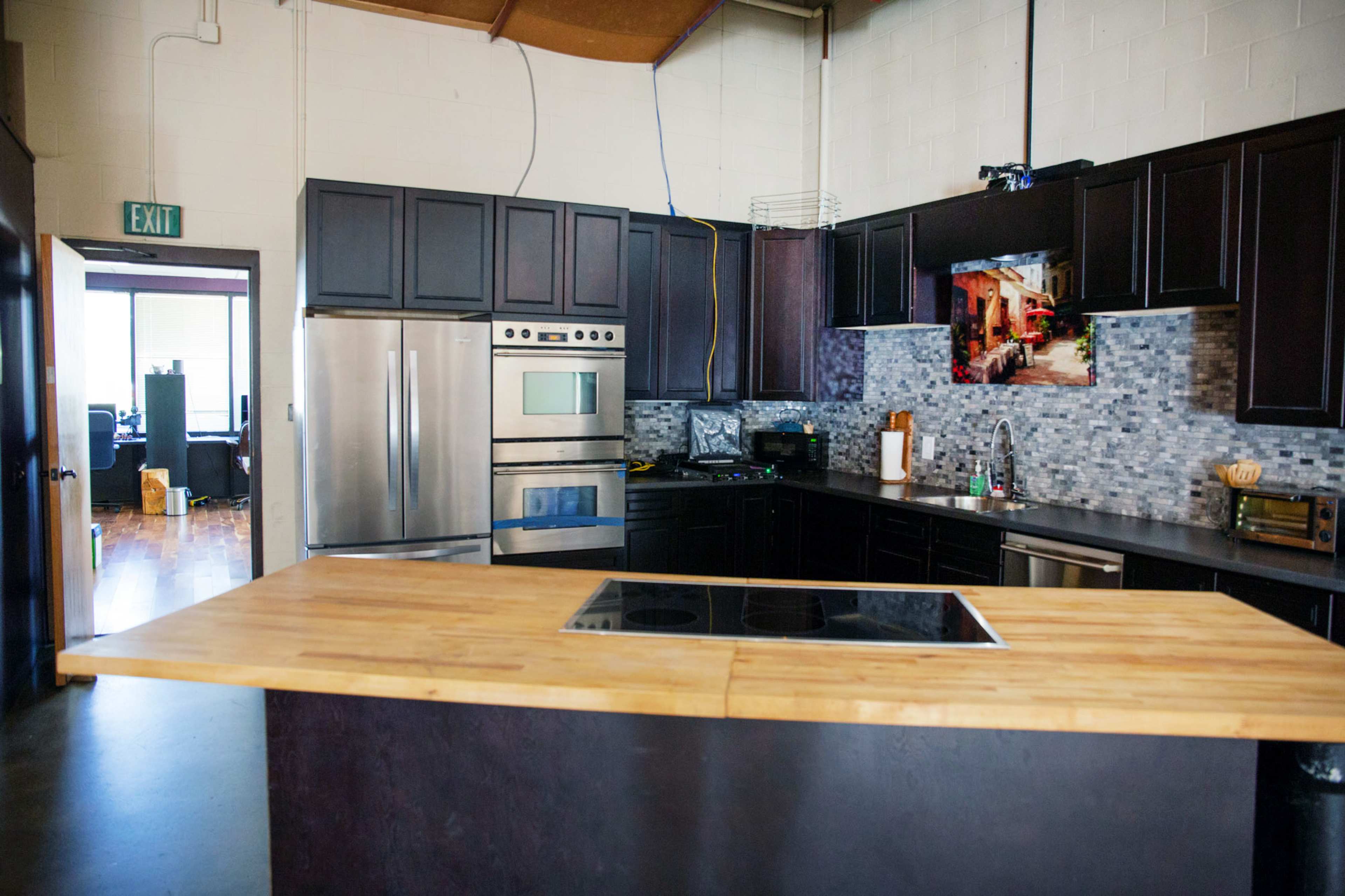 A modern kitchen features dark cabinets, stainless steel appliances, and a large wooden island with a built-in cooktop.