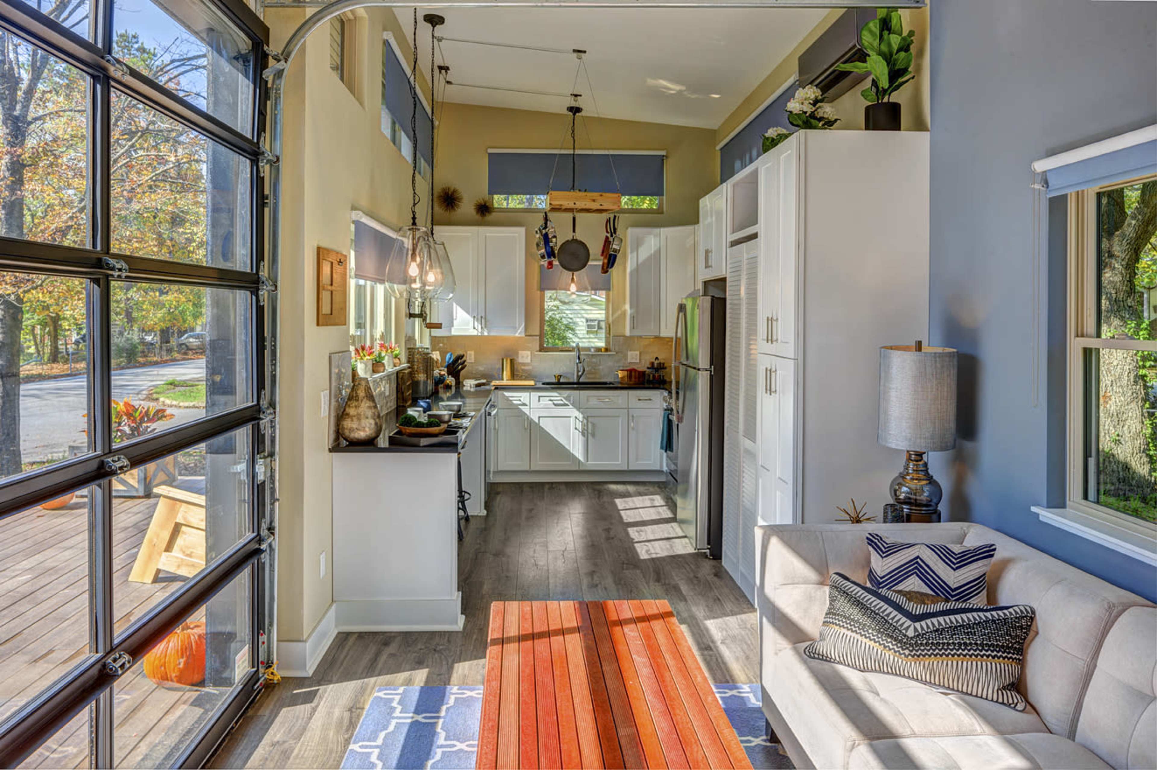A modern open-concept living space with a kitchen, dining area, and a cozy seating arrangement, featuring large windows and a garage door that opens to an outdoor deck.