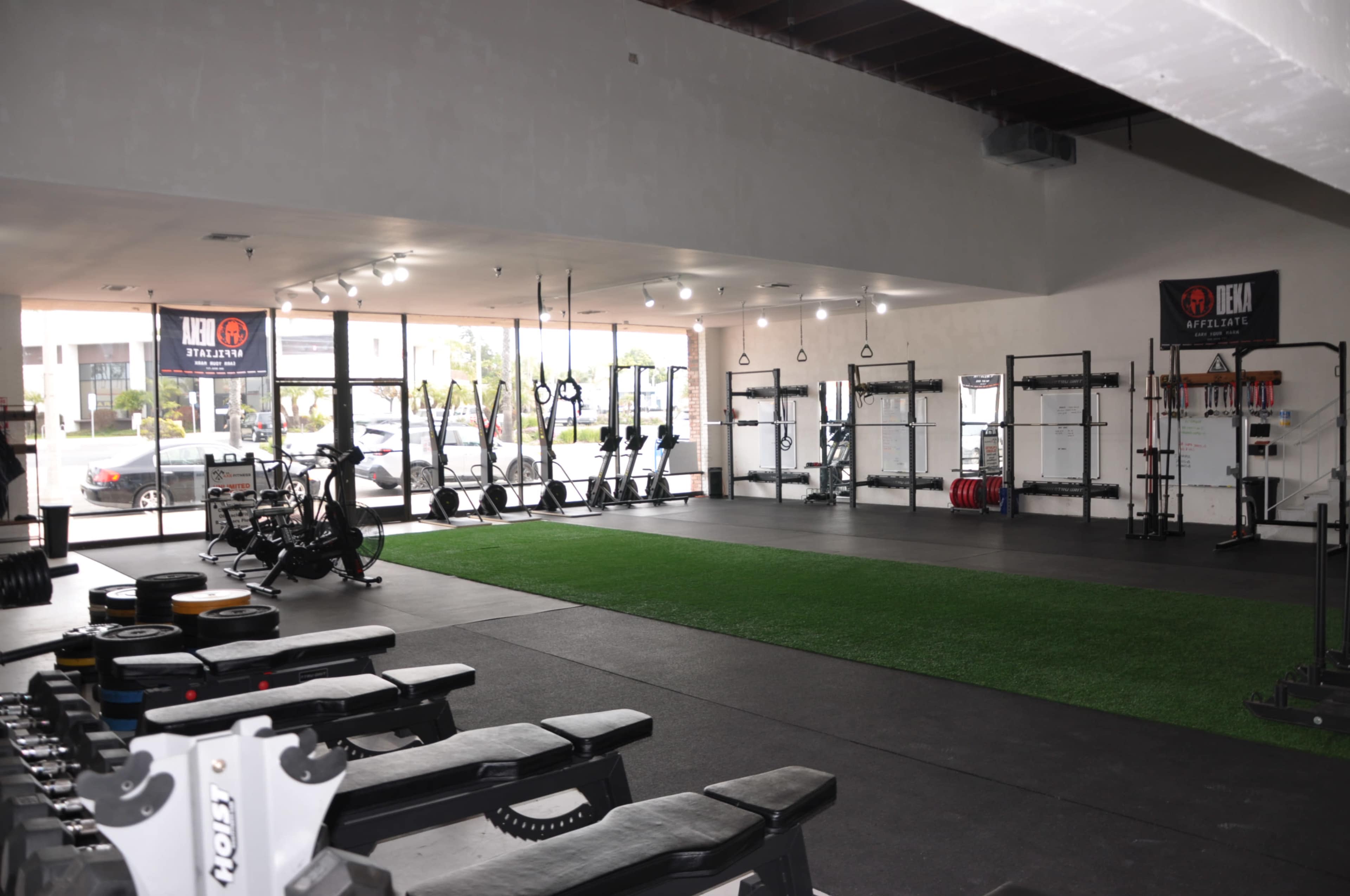 A spacious gym interior equipped with weightlifting benches, various exercise machines, and weight plates, featuring large windows that provide natural light.