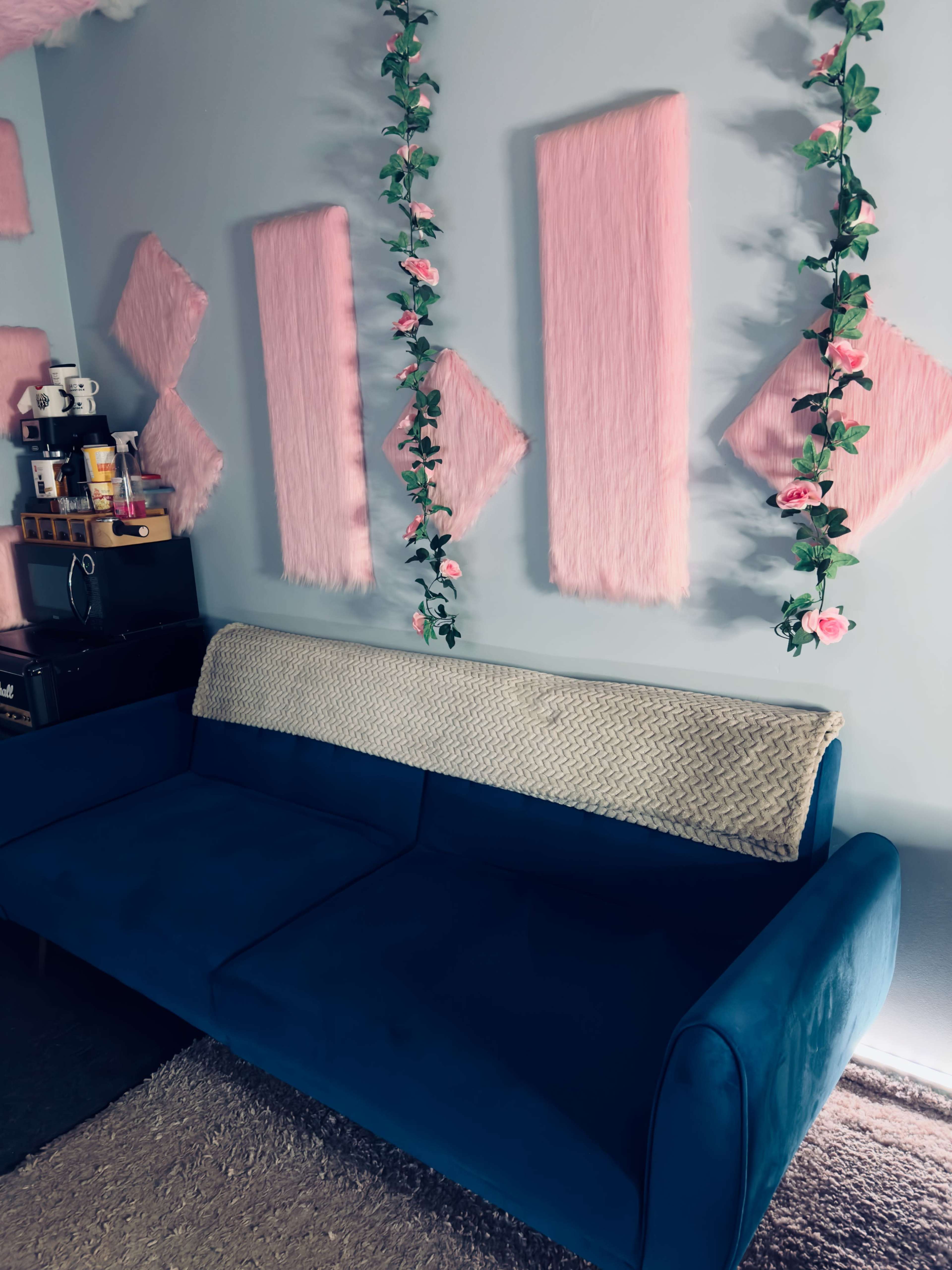 A blue couch against a light blue wall adorned with pink decorative panels and flower garlands.
