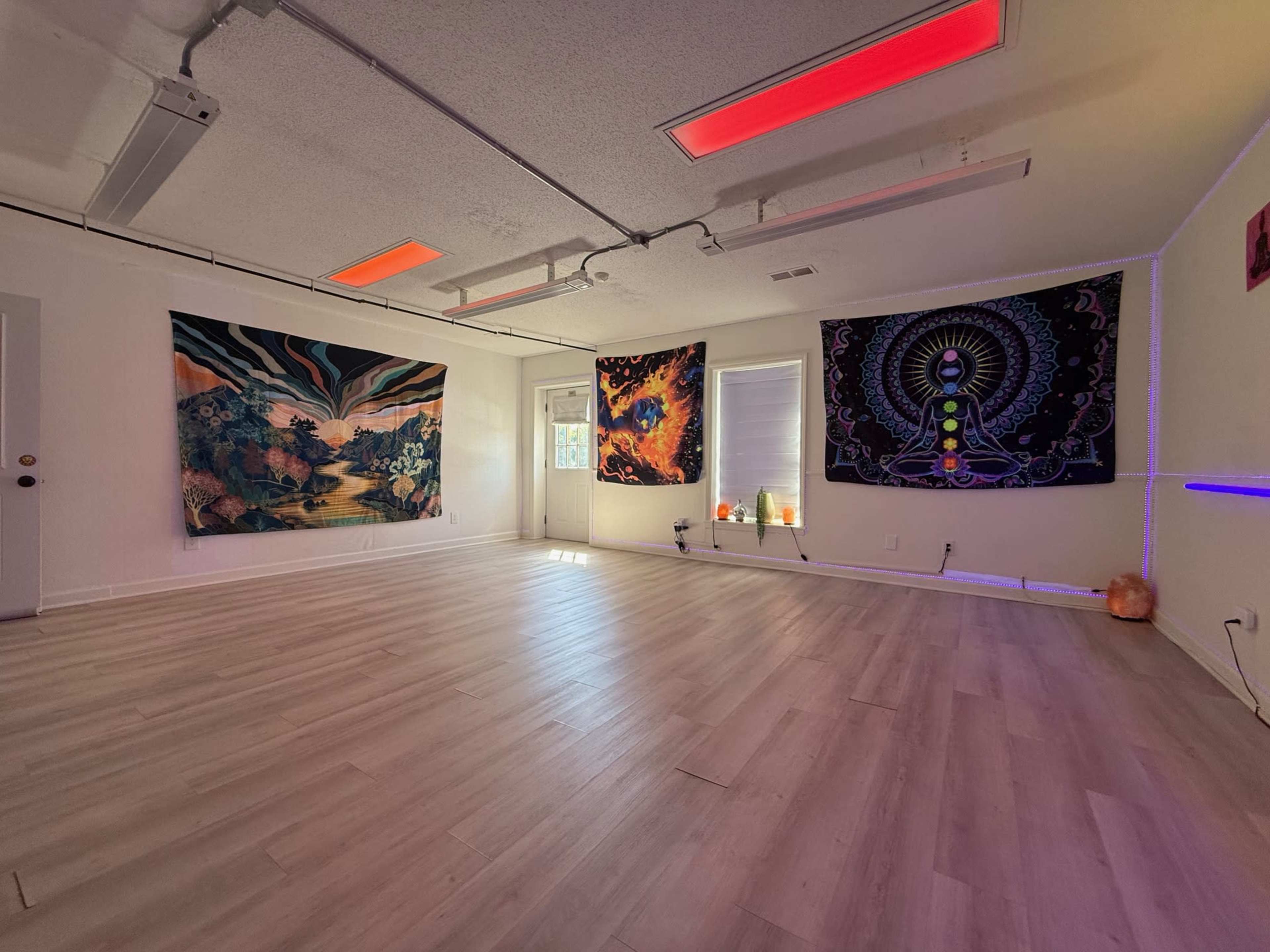 The image depicts a spacious room with light-colored flooring, featuring colorful wall tapestries and ambient lighting.