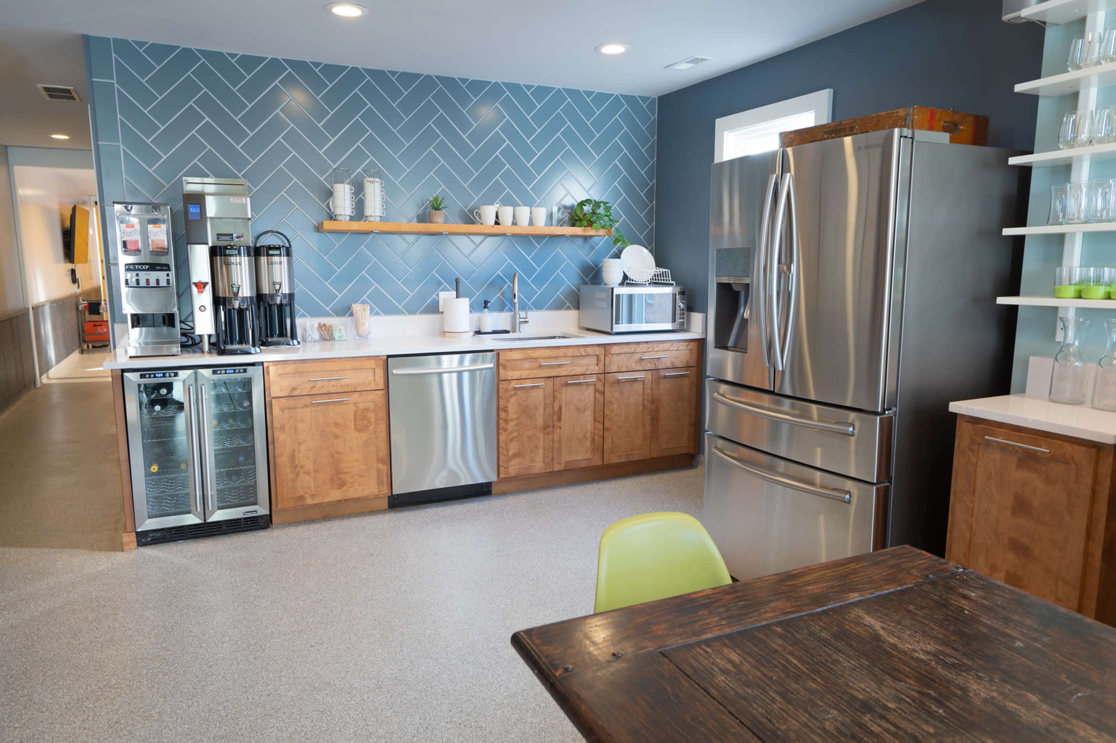 The image shows a modern kitchen with wooden cabinetry, stainless steel appliances, and a blue herringbone-patterned accent wall.