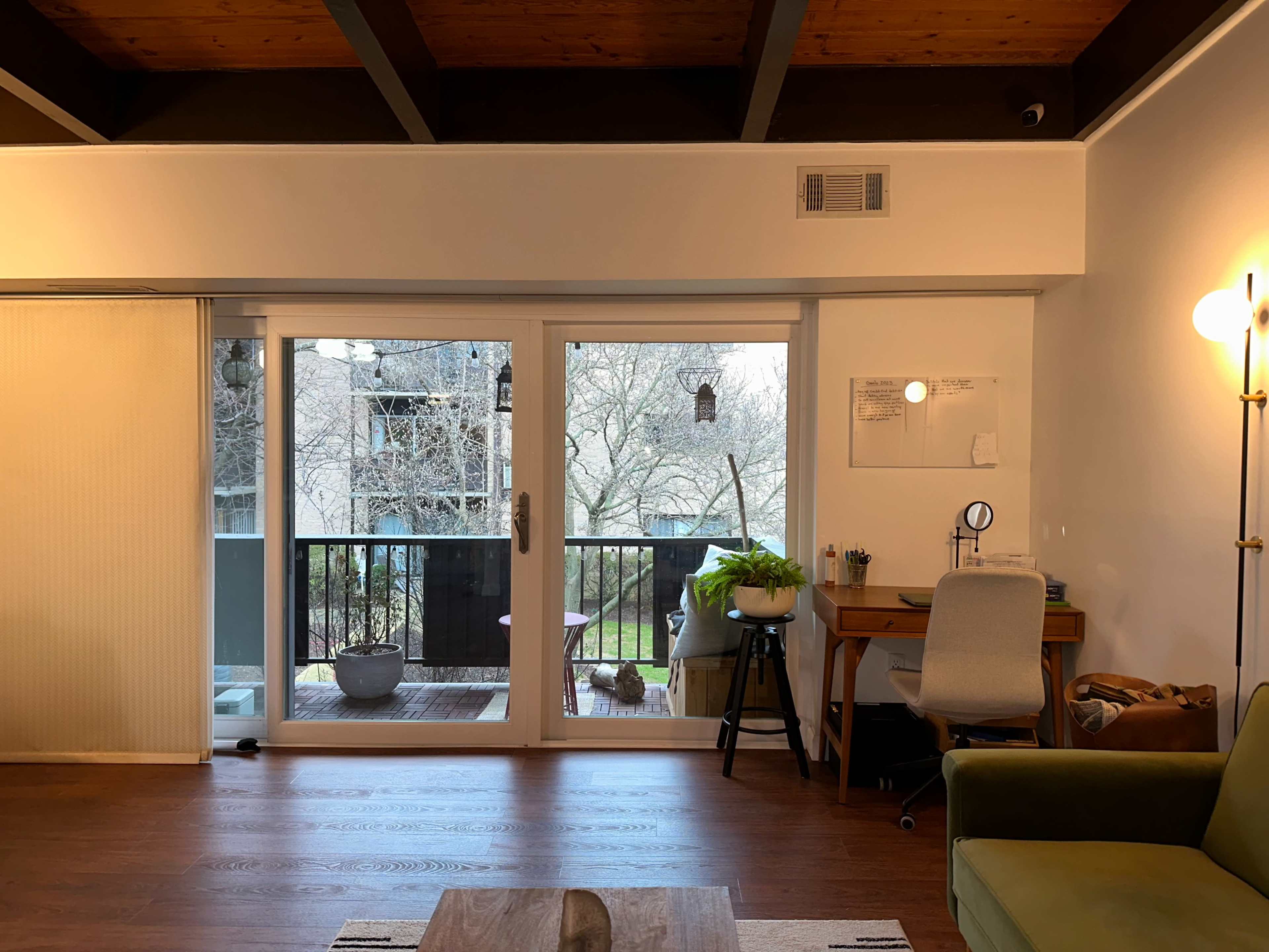 A cozy living room with large sliding glass doors leading to a balcony and a wooden desk and chair situated against the far wall.