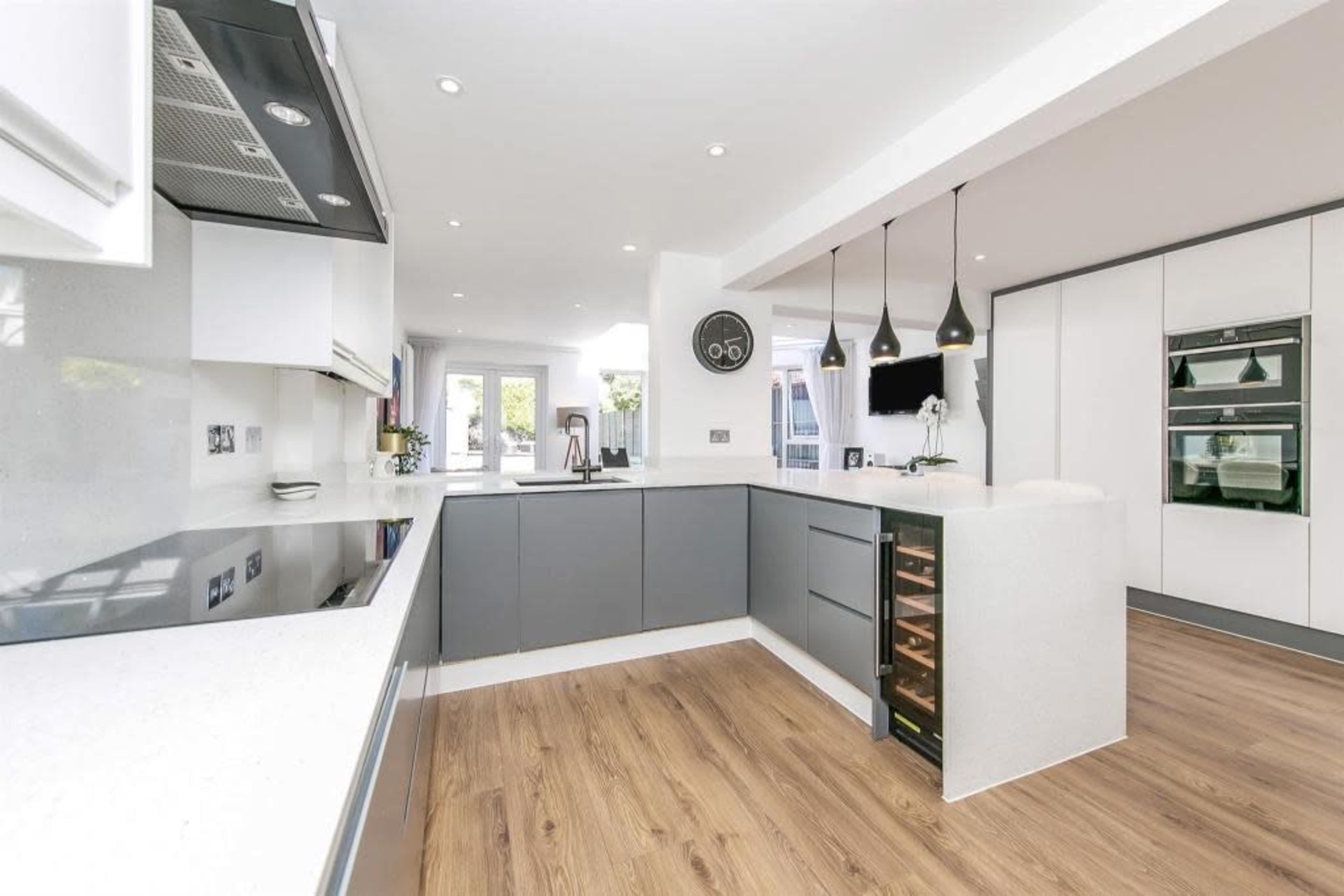 A modern kitchen with gray cabinetry, a white countertop, and wooden flooring, featuring built-in appliances and pendant lighting.