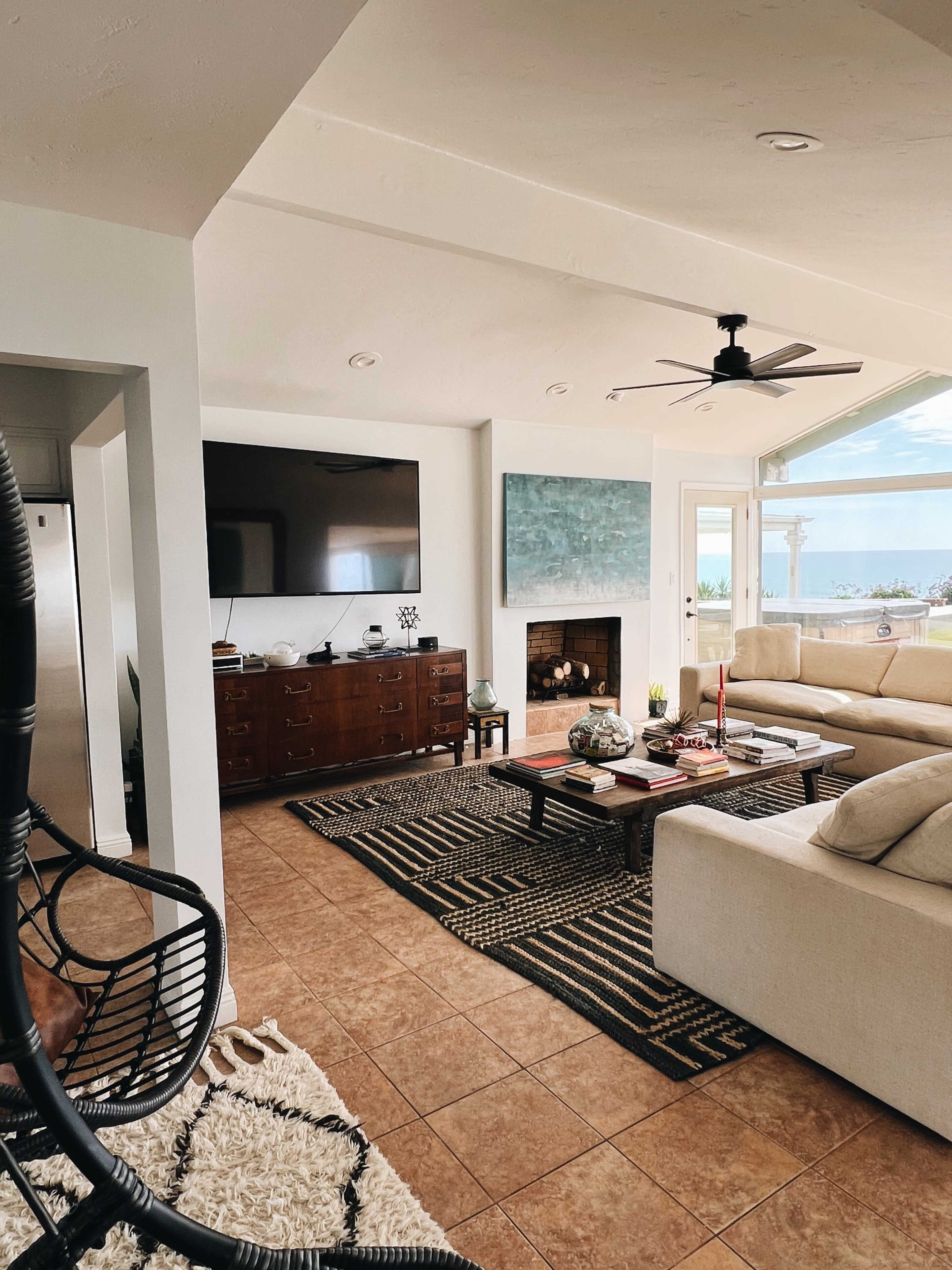 The image shows a modern living room with a large television mounted on a wall, a wooden sideboard, and a sectional couch arranged around a coffee table on a patterned area rug.