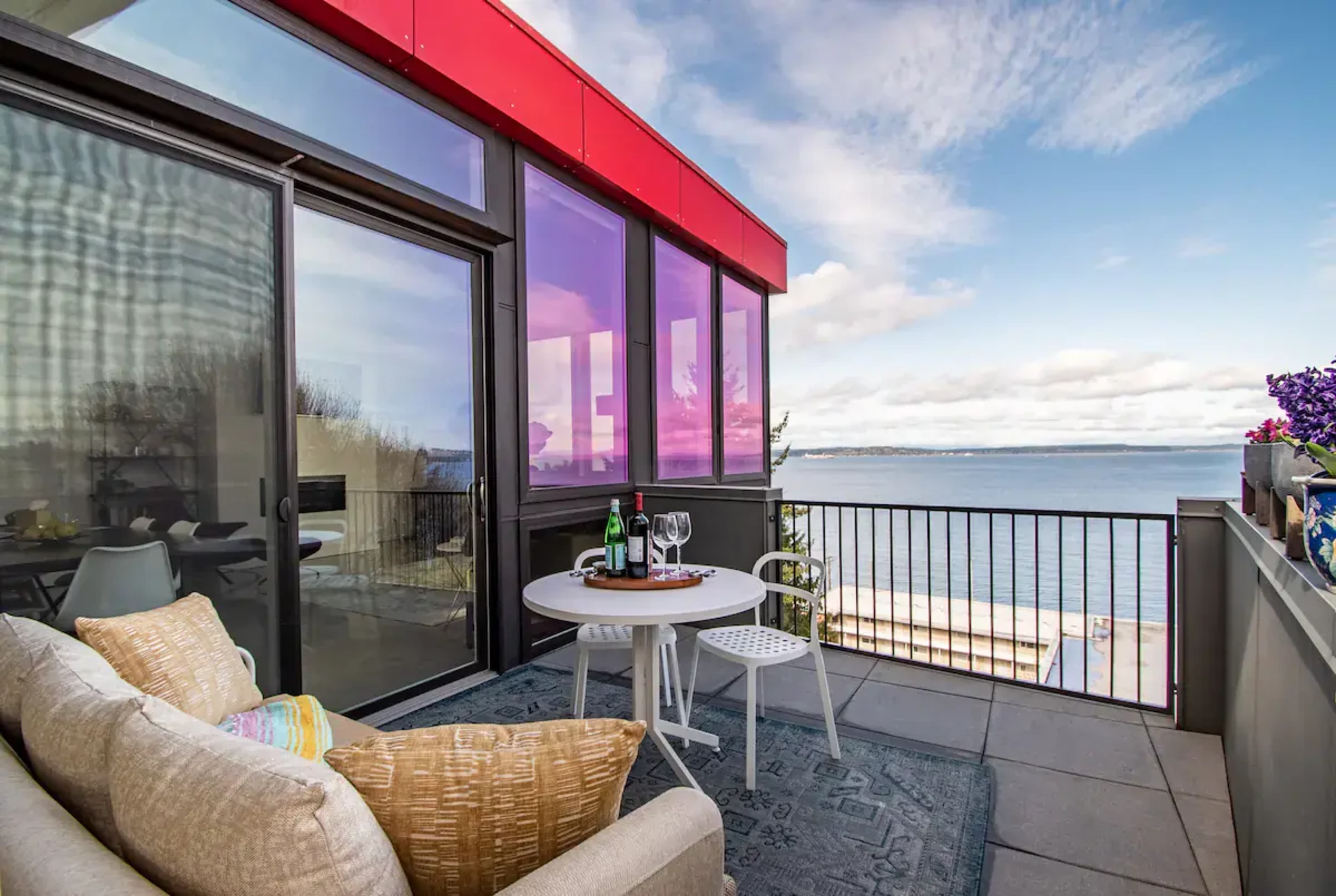 A balcony with a small table and chairs overlooks a body of water under a partly cloudy sky.