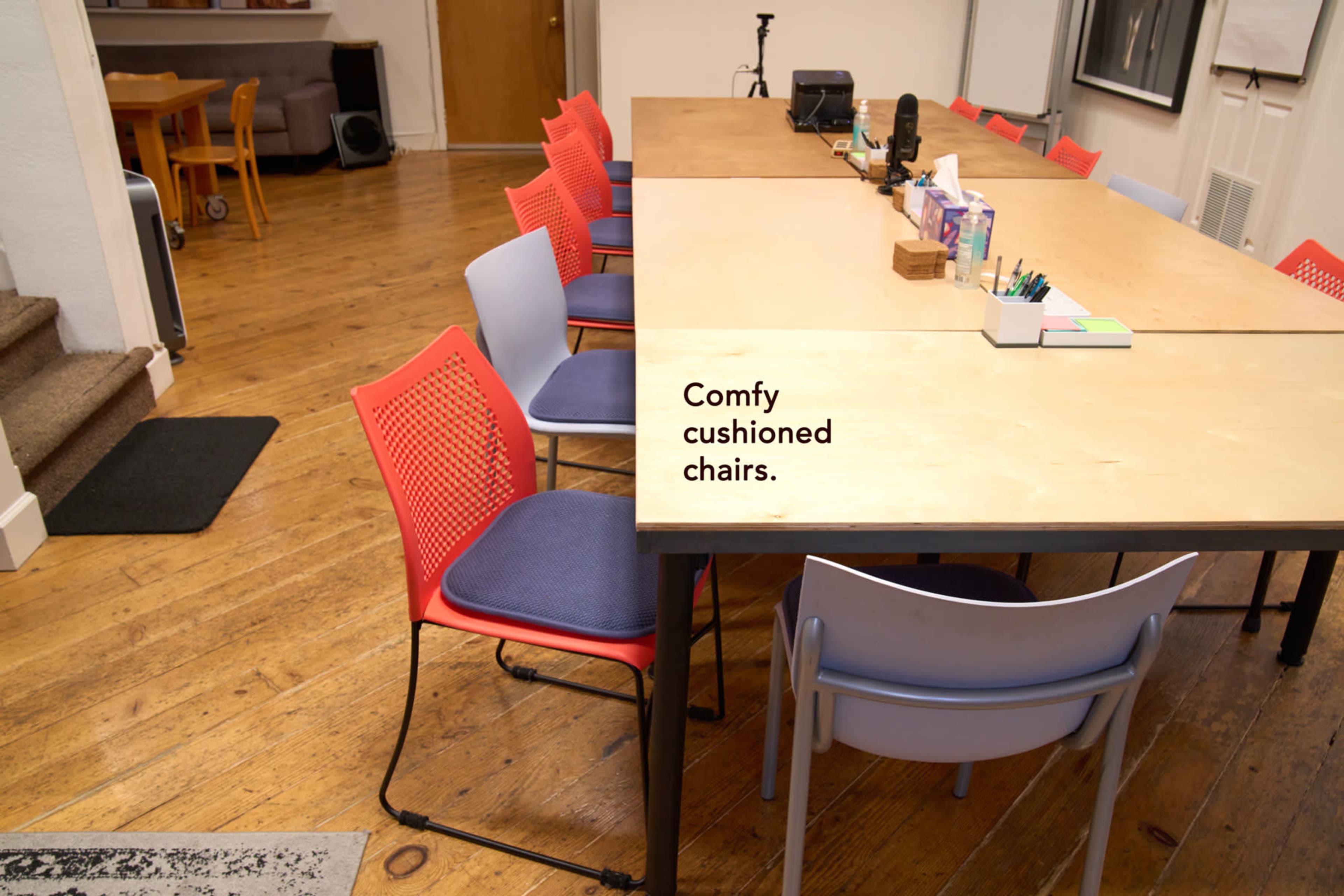 A large wooden table is surrounded by colorful cushioned chairs in a room with wooden flooring.