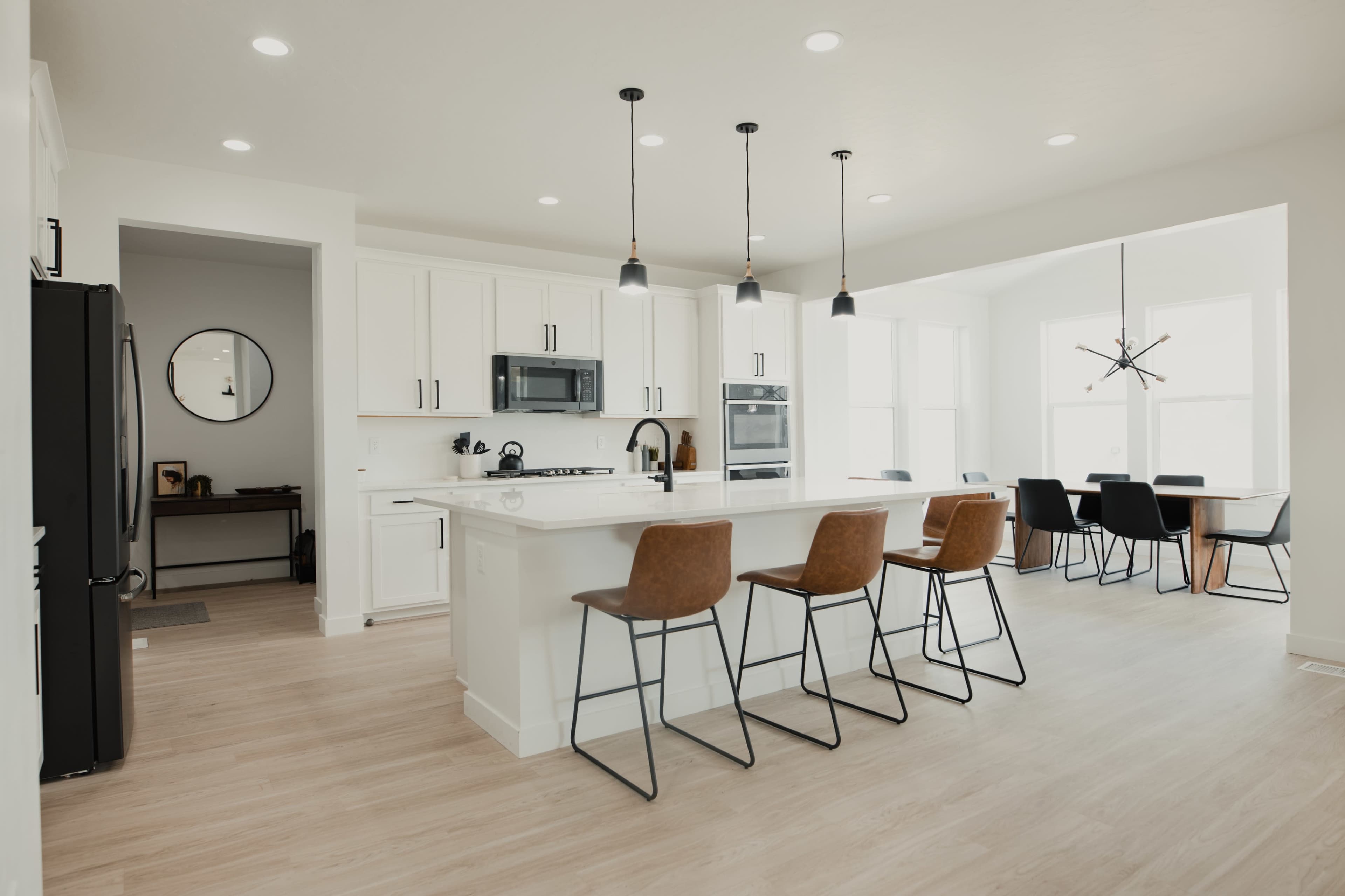 A bright kitchen features a central island with seating, modern appliances, and an open dining area with large windows.