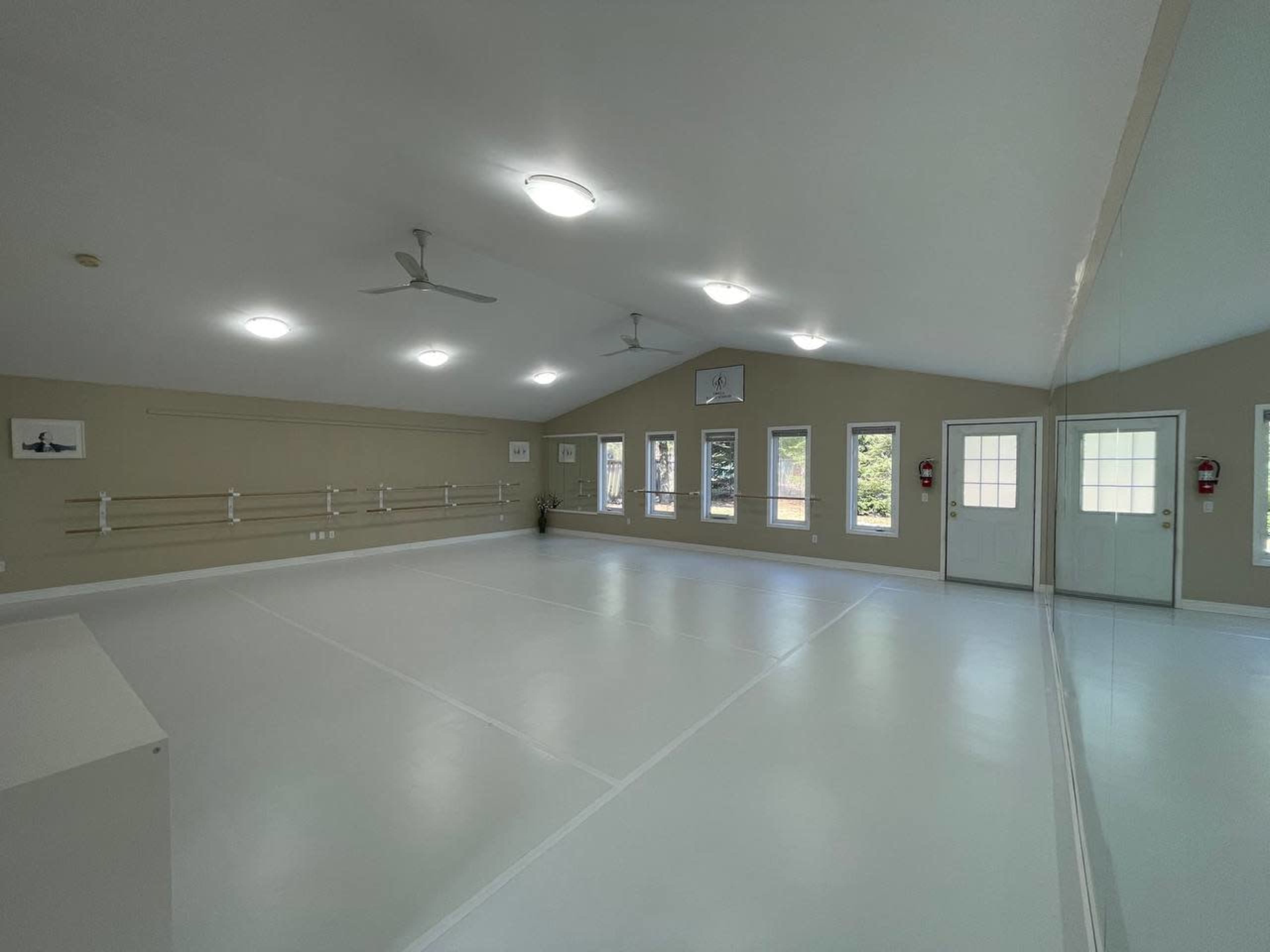 A spacious, well-lit dance studio with mirrored walls and large windows.
