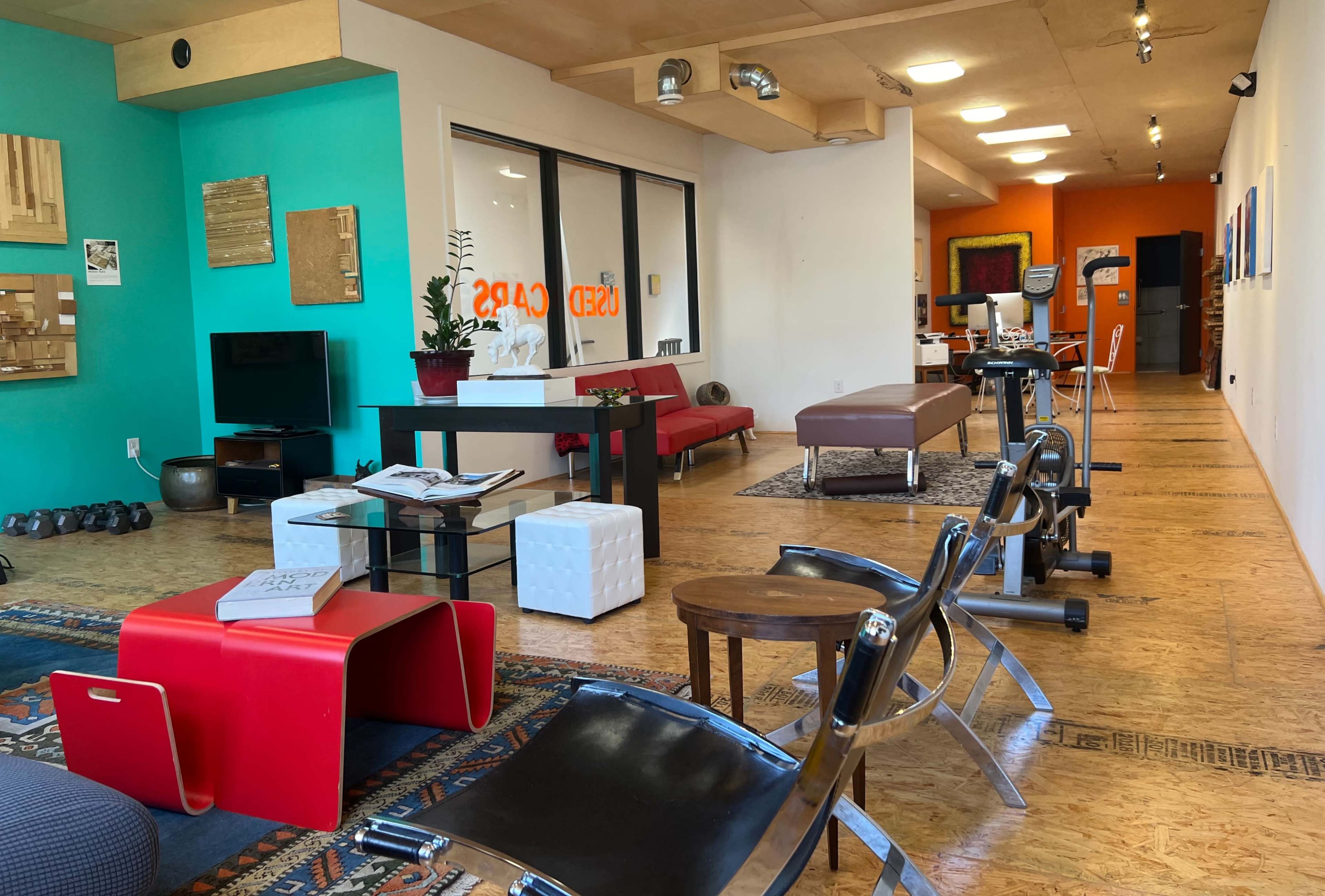 A well-lit modern interior space featuring a mix of exercise equipment, seating areas, and decorative elements on the walls.